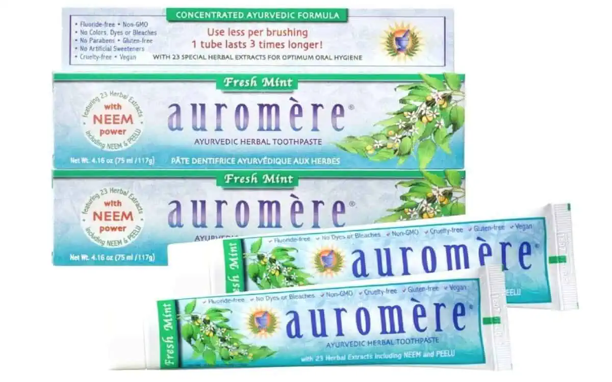 Two tubes of Auromere toothpaste in blueish green tubes laying in front of 2 stacked boxes of Auromere.