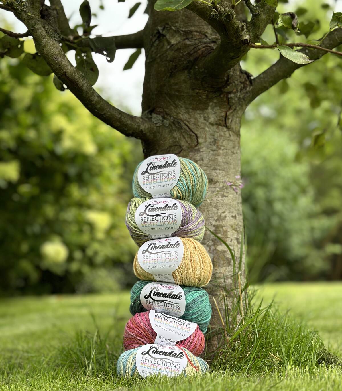 Six skeins of vegan yarn from the Earth Yarns website in a standing pile up against a shaded tree.