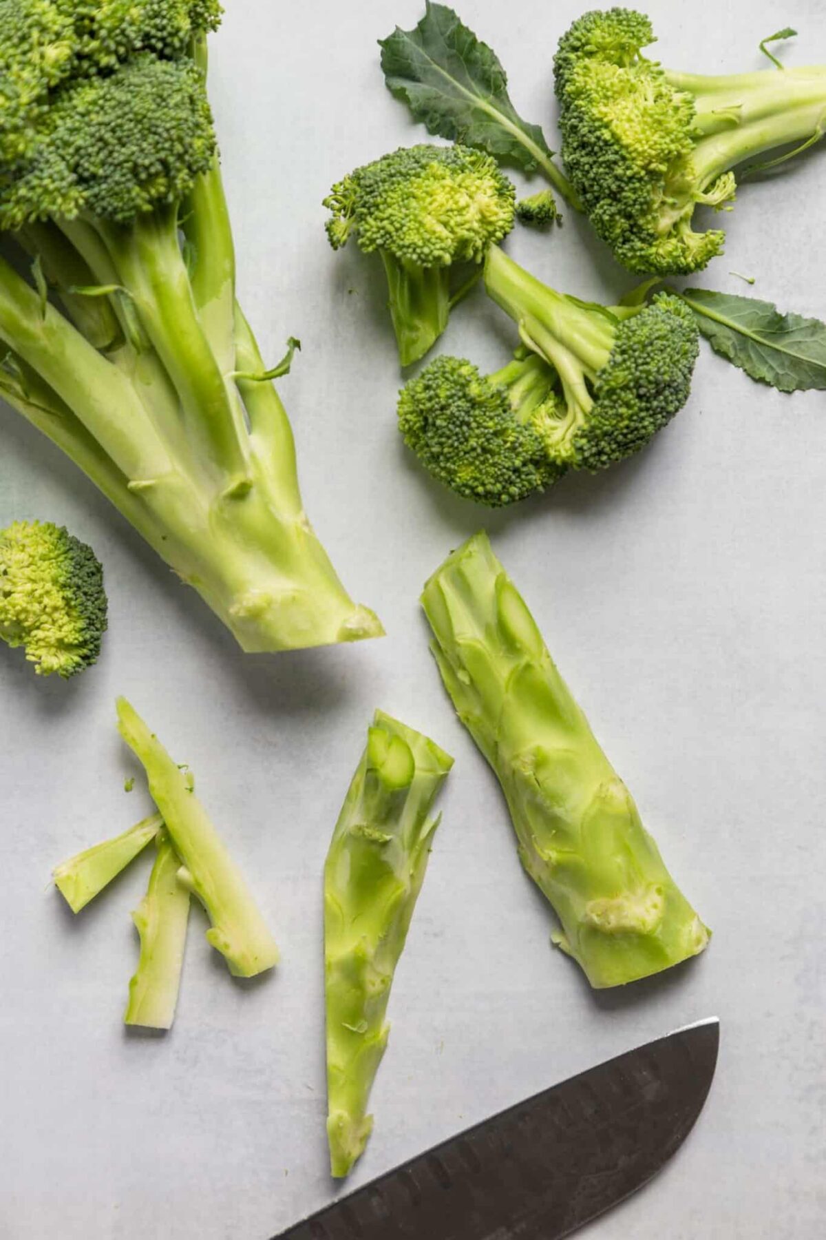 Broccoli stalks chopped on a cutting board with a chefs knife.
