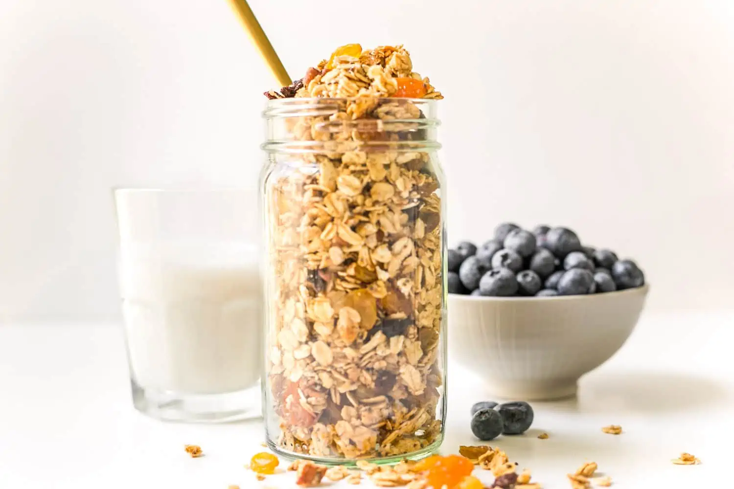 Large mason jar filled with vegan homemade granola and a bowl of fresh blueberry