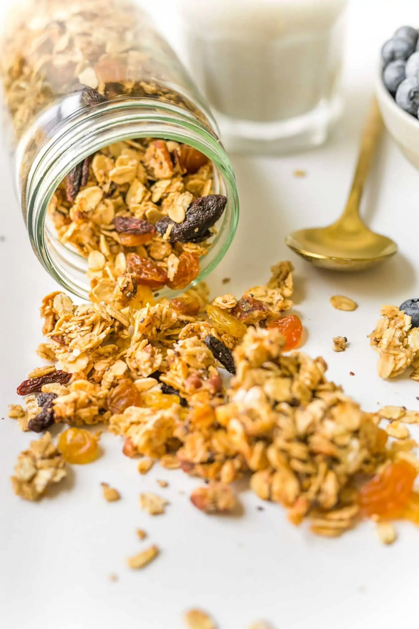 Mason jar filled with homemade granola spilled on white surface.