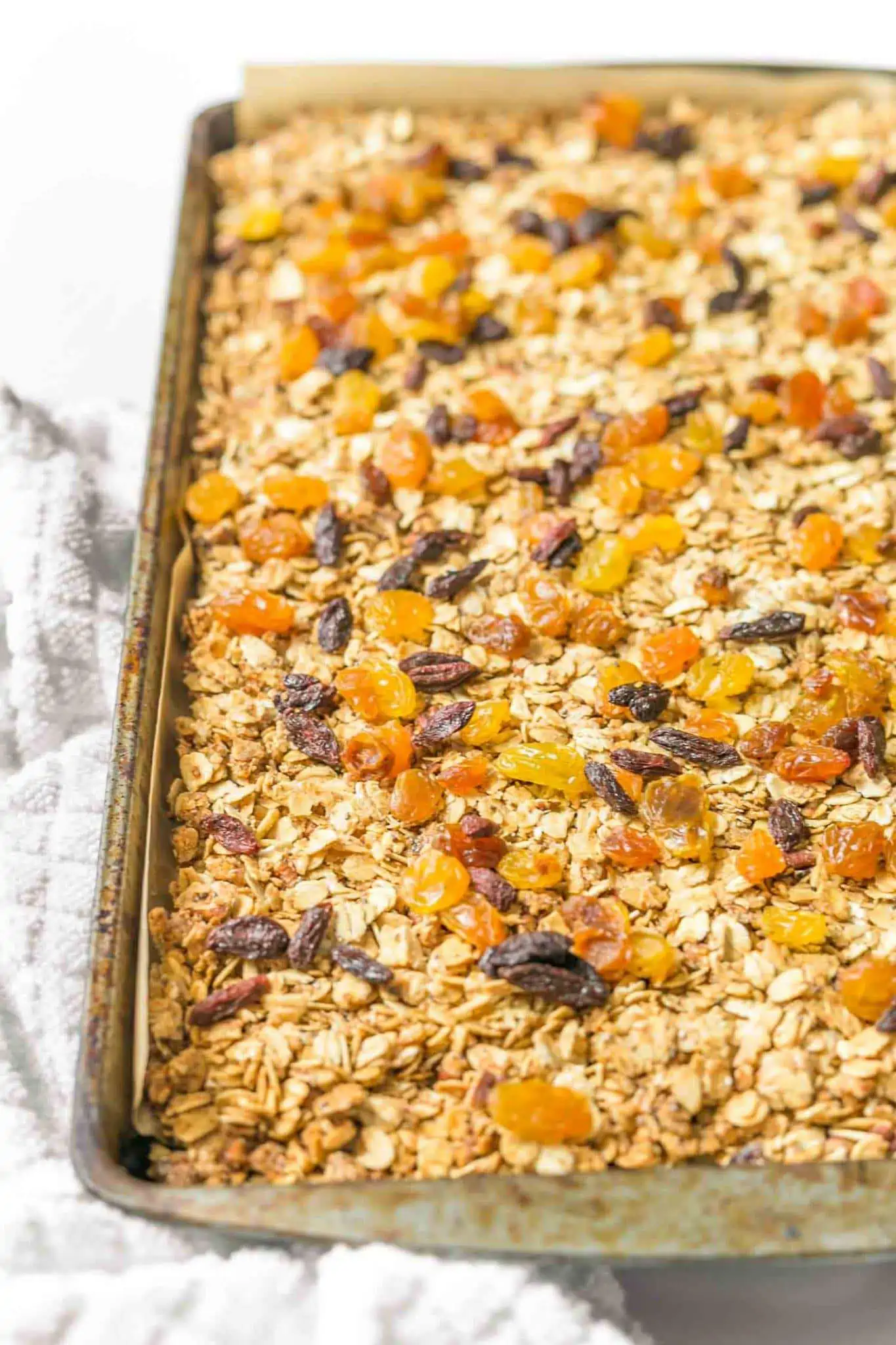 A baking tray of vegan granola with raisins and goji berries sprinkled on top.