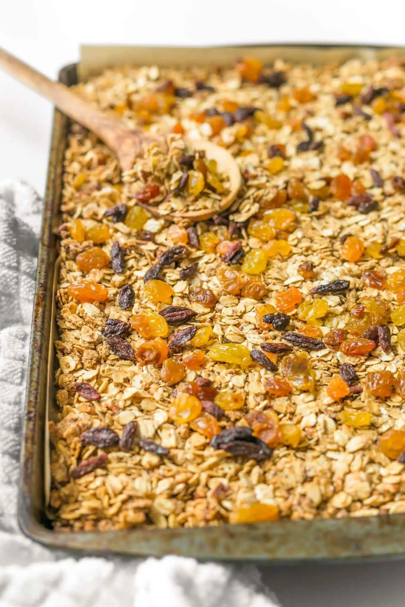 Baking tray with vegan homeamde granola with a large wooden spoon on a white surface