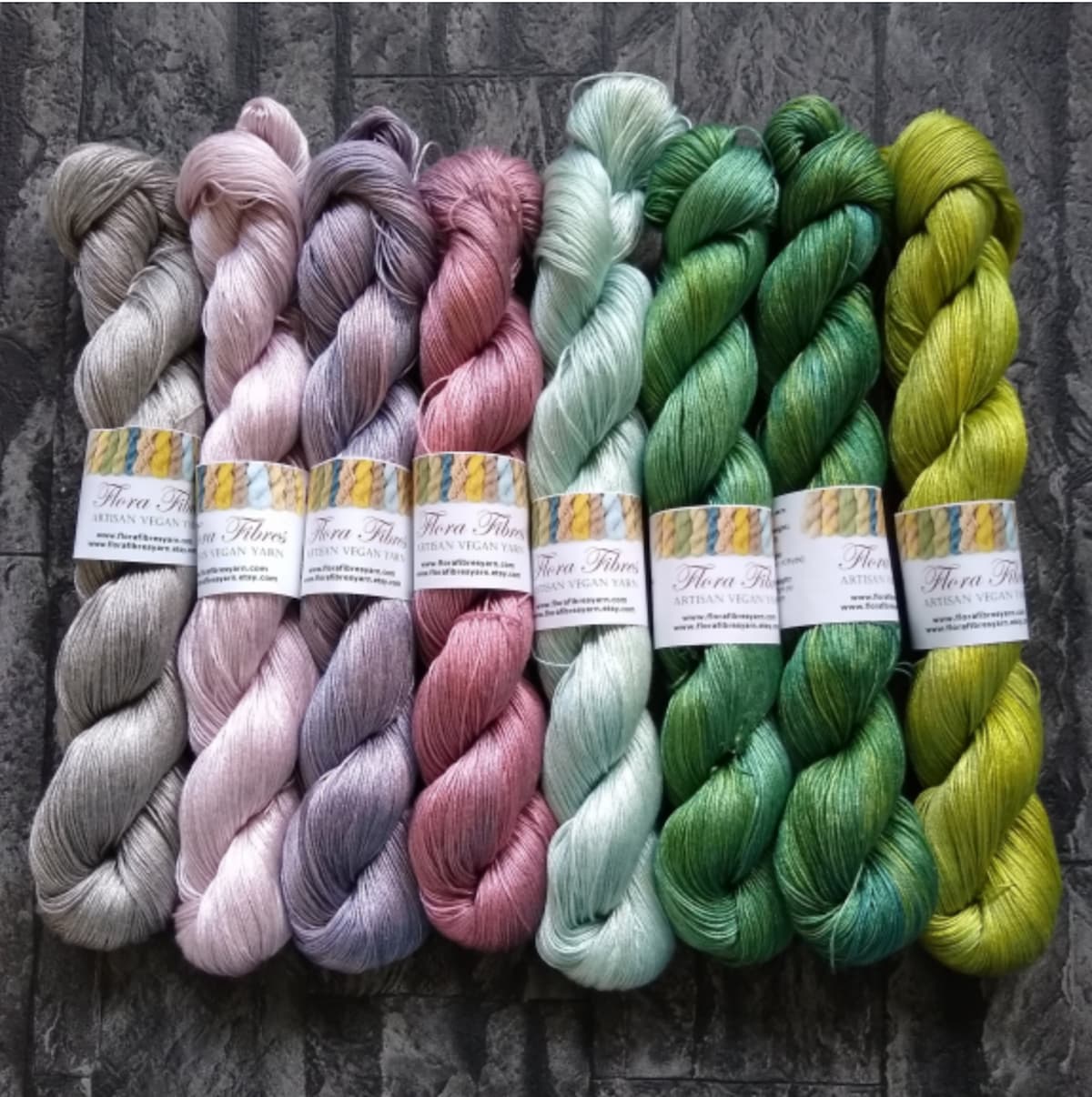 Muted spring colored skeins of Flora Fibres vegan yarn on a gray wooden background.