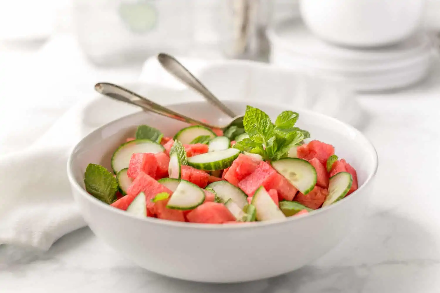 Watermelon cucumber salad in a big serving bowl with serving utensils.