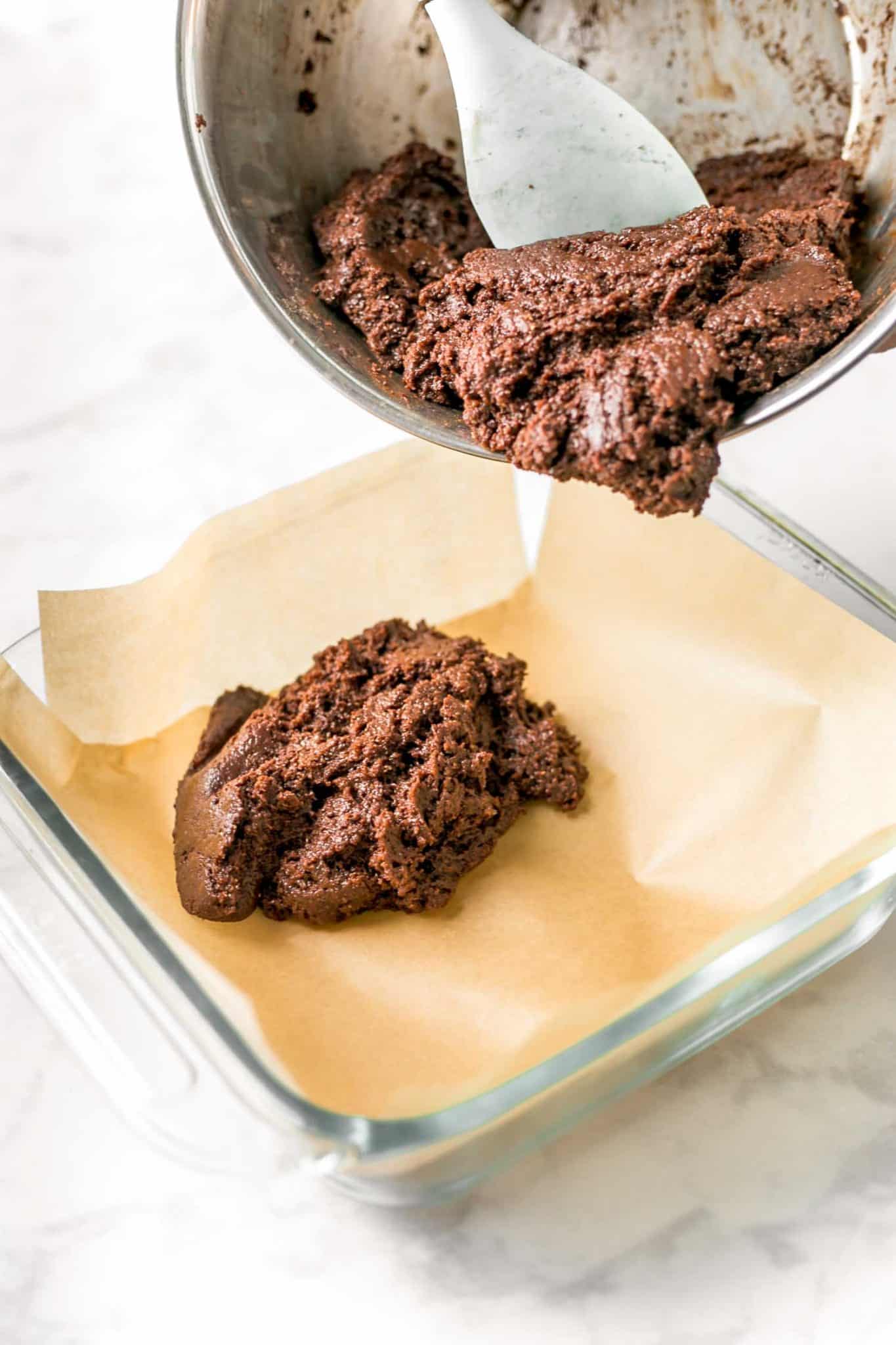 Brownie batter being transferred to a parchment-lined glass baking dish.