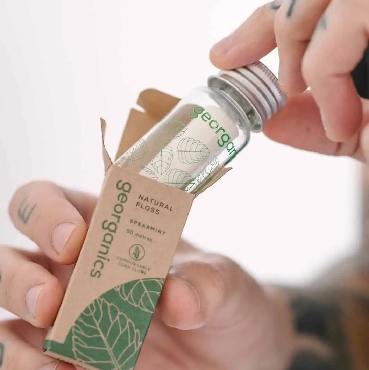 Hands pulling out a glass bottle of Georganics vegan floss out of a small cardboard box.