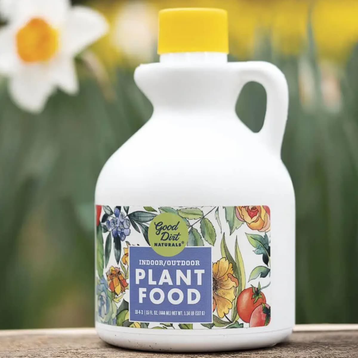 A plastic jug of Good Dirt Naturals liquid vegan fertilizer against a background of white and yellow daffodils.