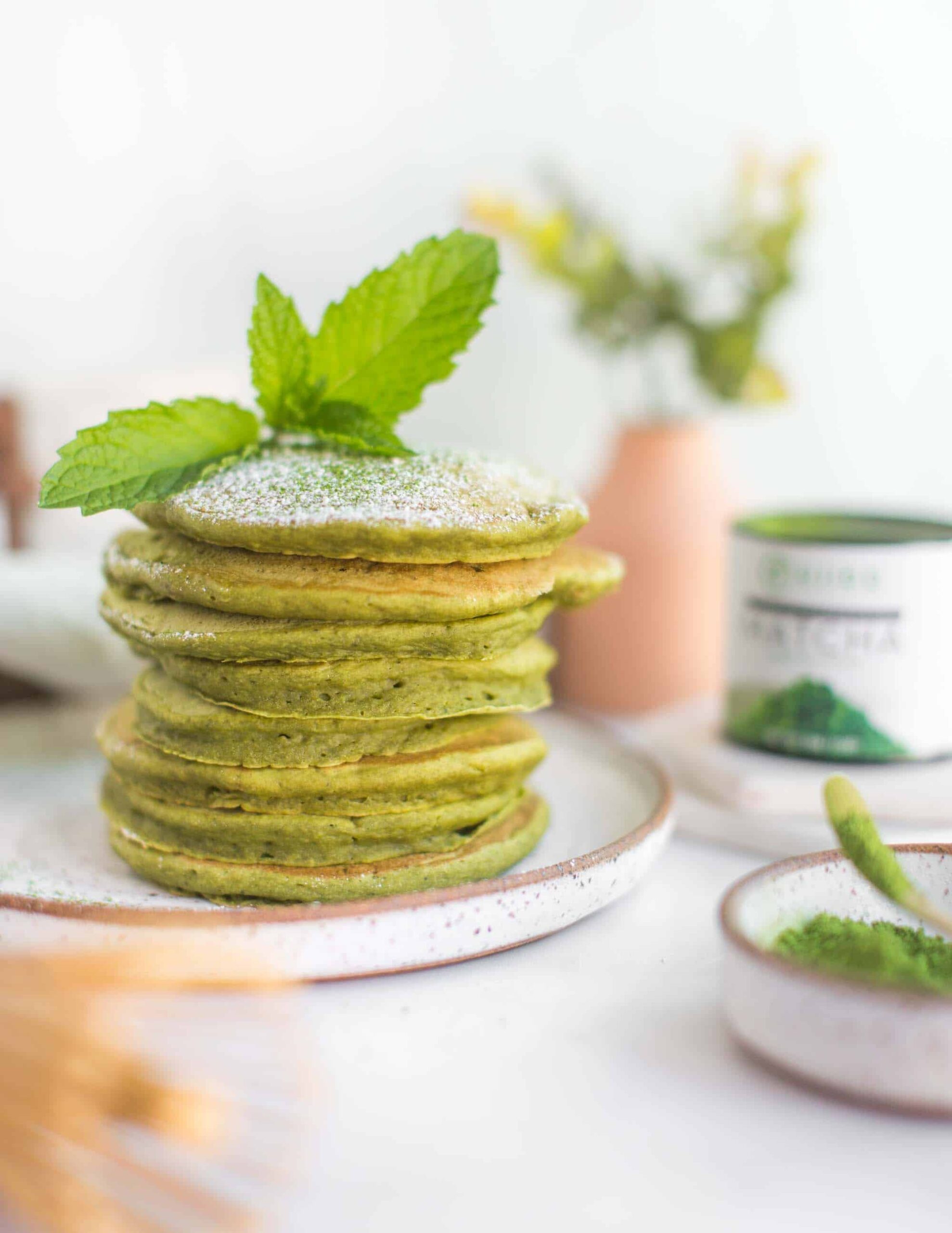 Stack of Green Vegan Matcha Pancakes With Powdered Sugar and a Mint Leaf.