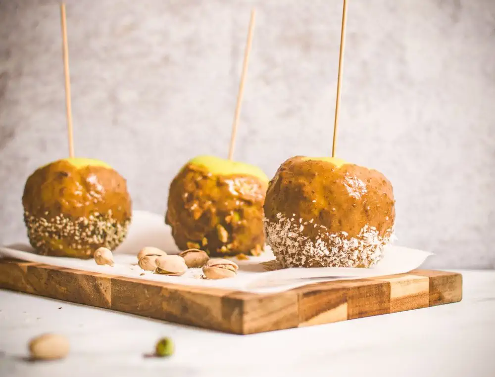 Homemade vegan caramel apples on sticks on a cutting board with pistachios.