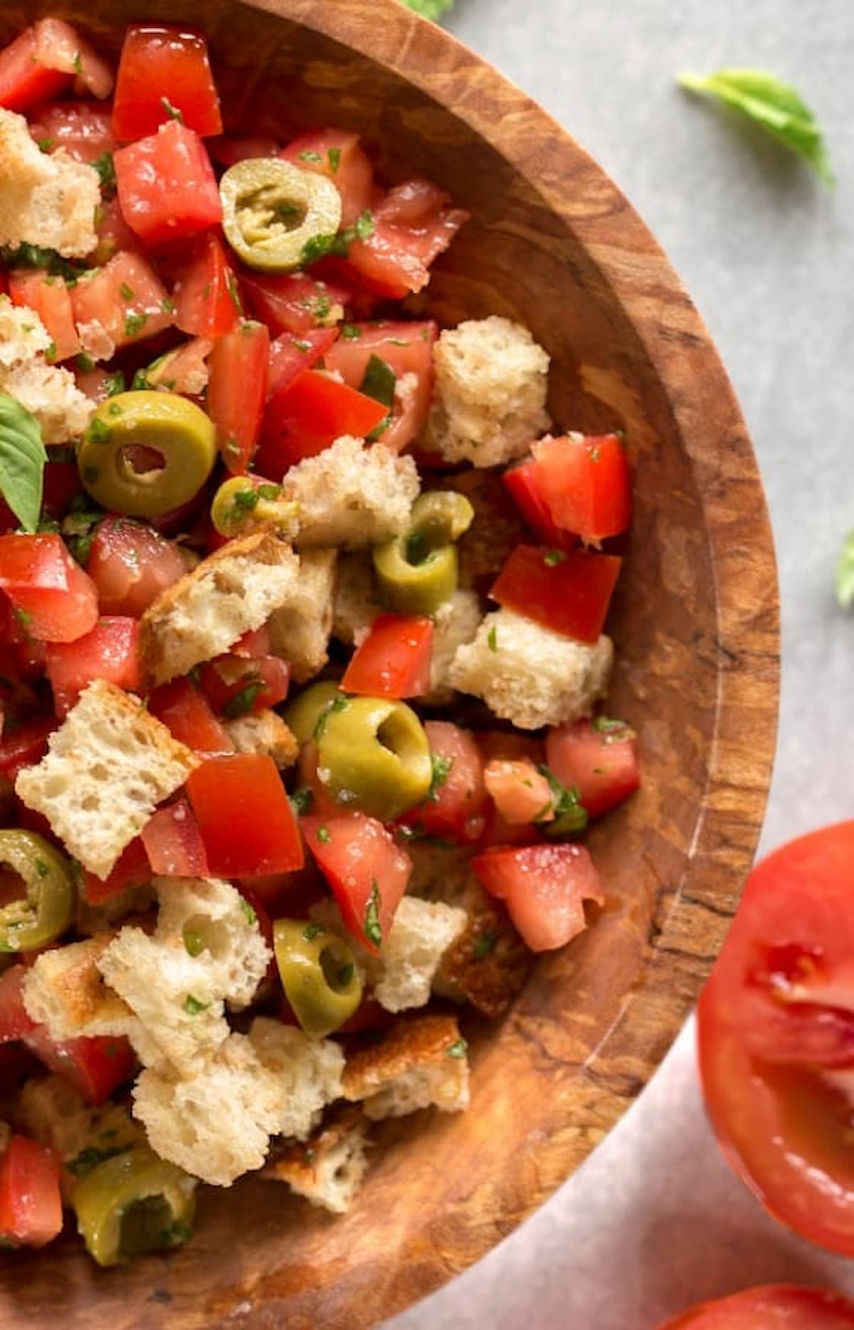 Italian tomato salad in a large wooden bowl with olives, fresh basil, and Italian bread.