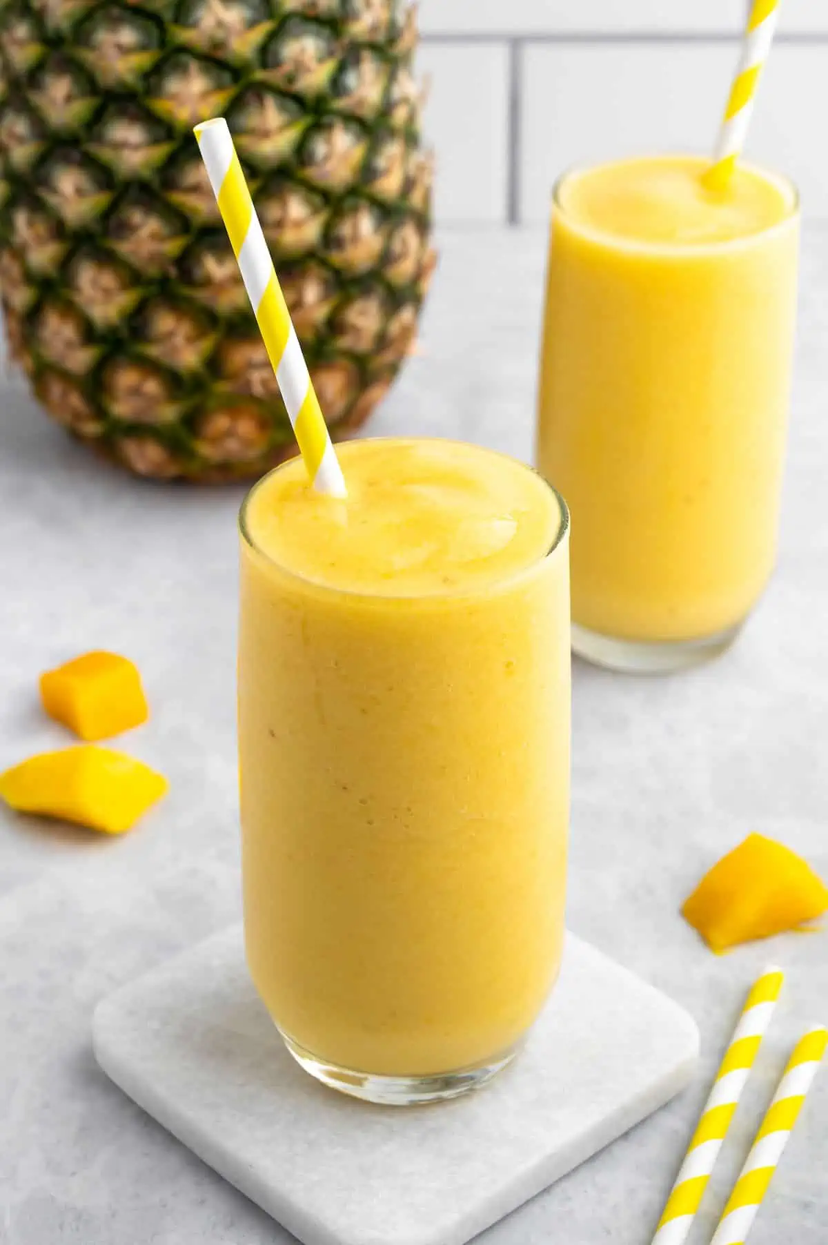 Two mango-pineapple smoothies with straws served in glasses—sweet, tropical, and dairy-free.