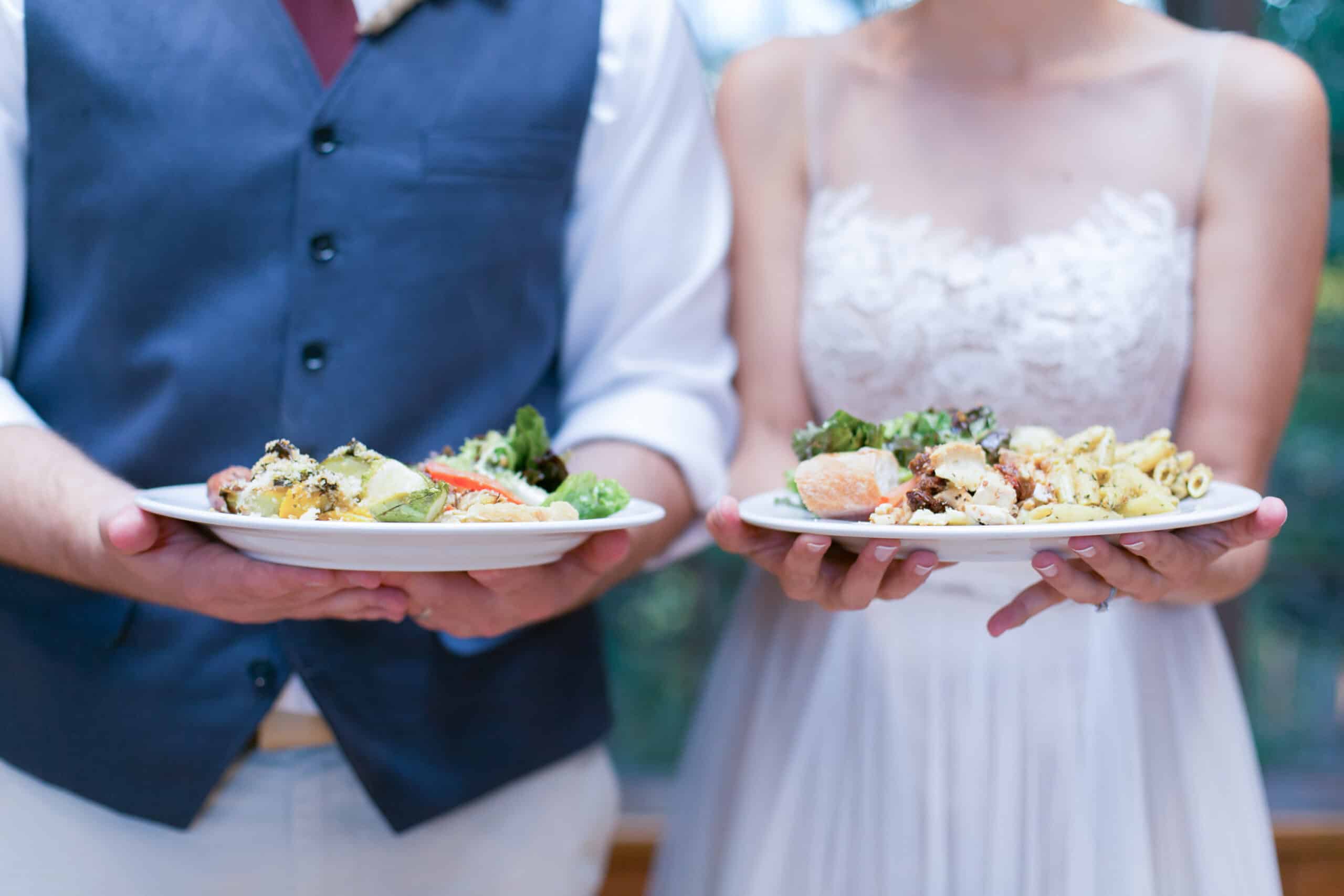 Close-up of bride and groom holding plates of vegan wedding food.