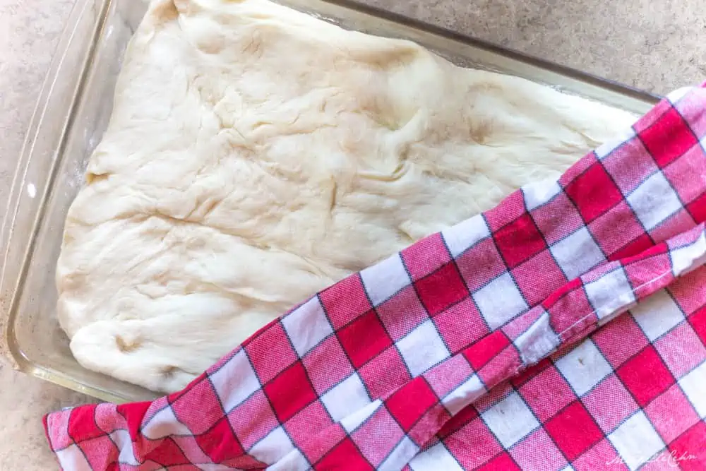 Focaccia bread dough rising with checkered cloth on top.