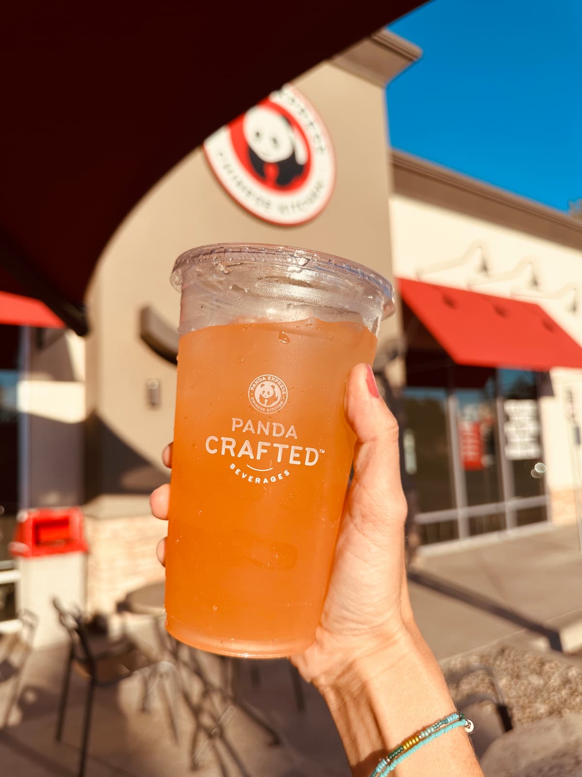 A hand holding a vegan-friendly beverage outside of Panda Express.