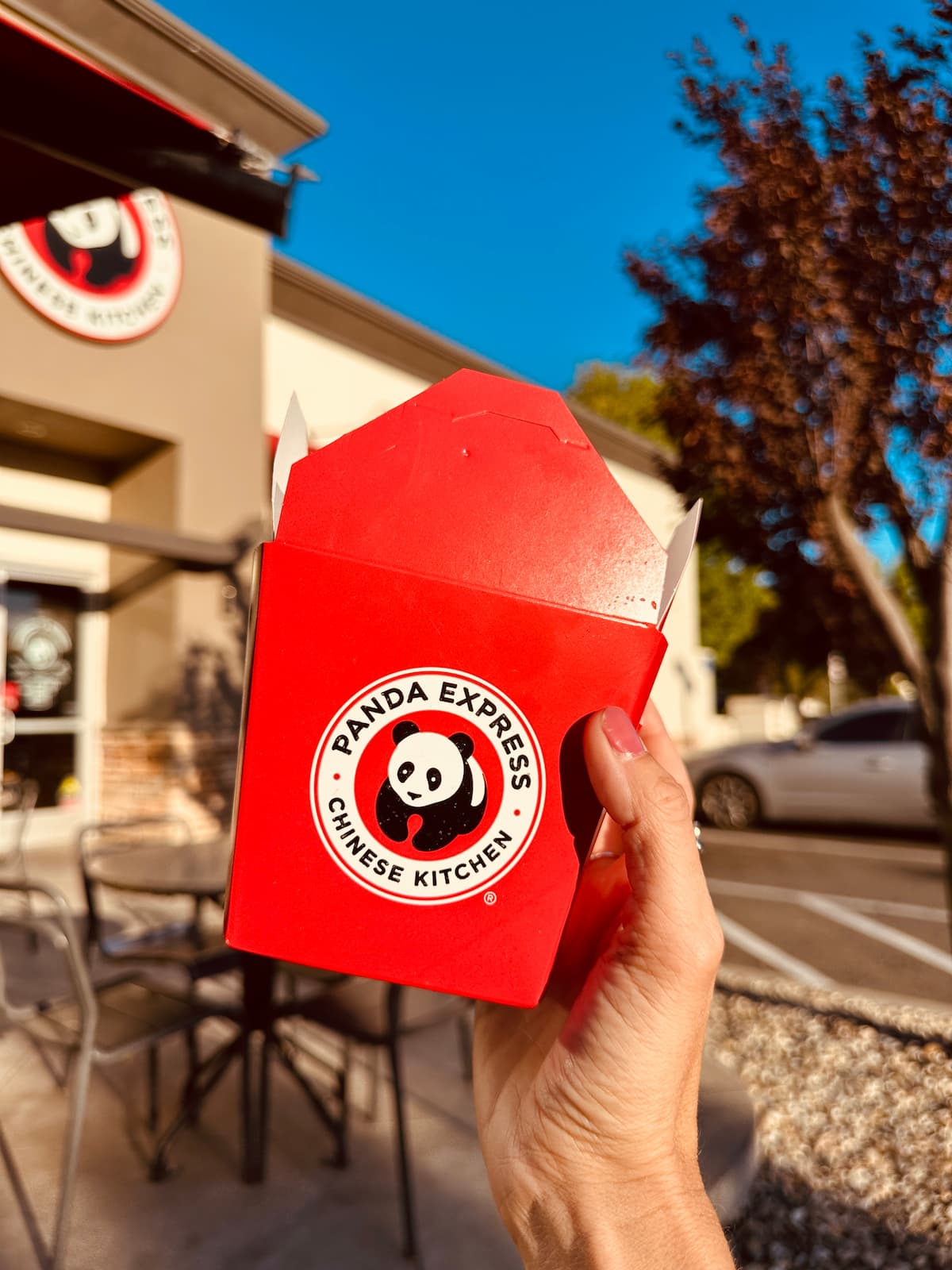 Panda Express take out container held in front of Panda Express restaurant.