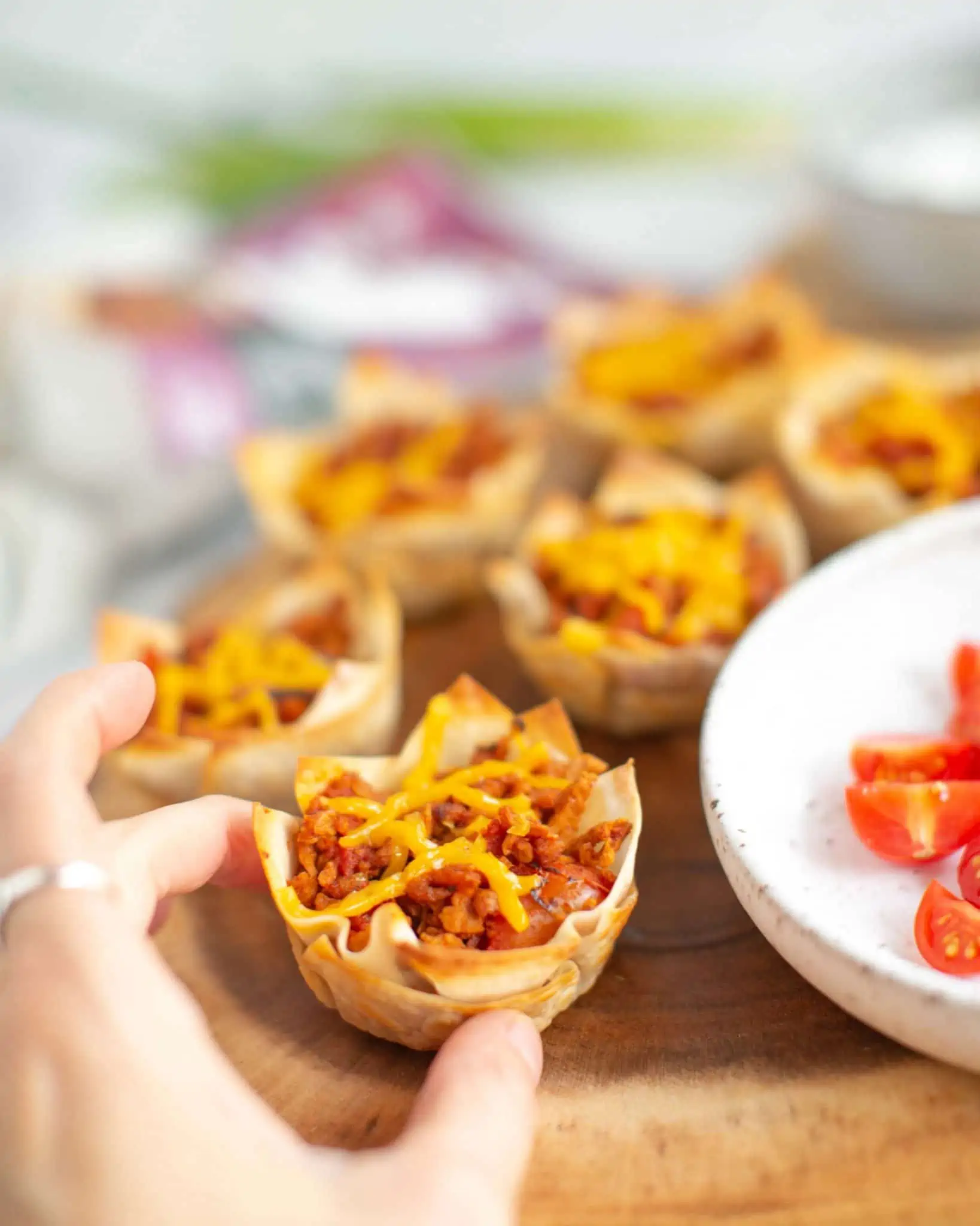 A hand reaching for a wonton taco cup that has just been baked.