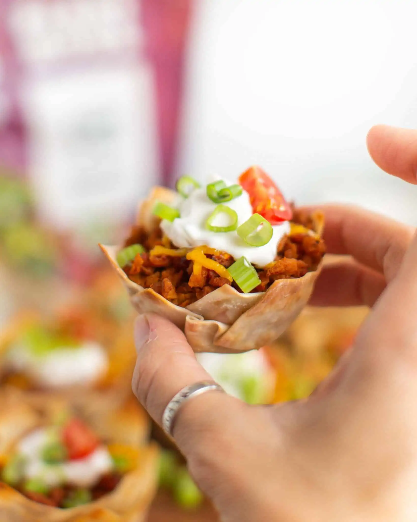 A hand holding up a vegan taco cup topped with vegan sour cream and sliced green onions.