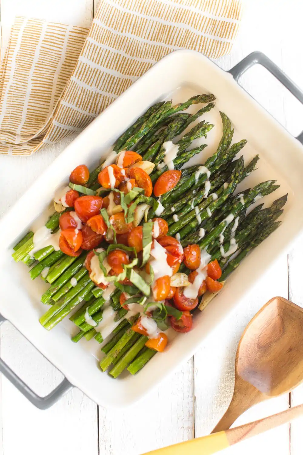 Casserole dish filled with sheet pan roasted asparagus, tomatoes, garlic, and a drizzle of tahini dressing.
