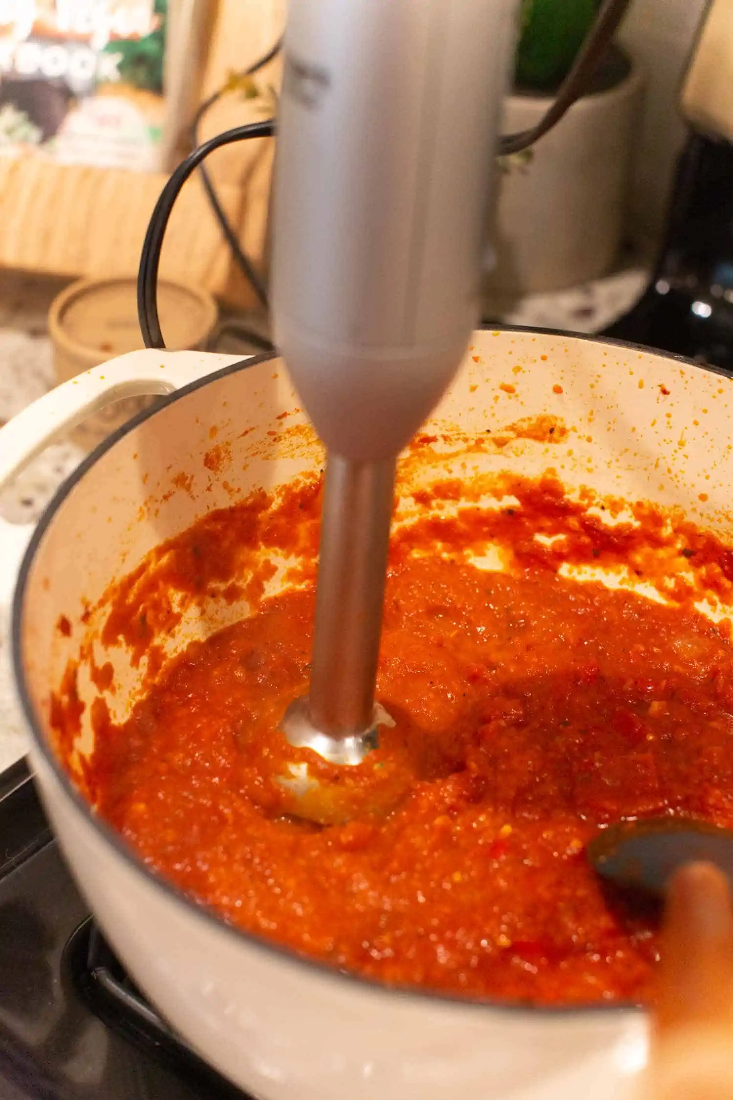 Blending arrabiata sauce with an immersion blender in a dutch oven pot.