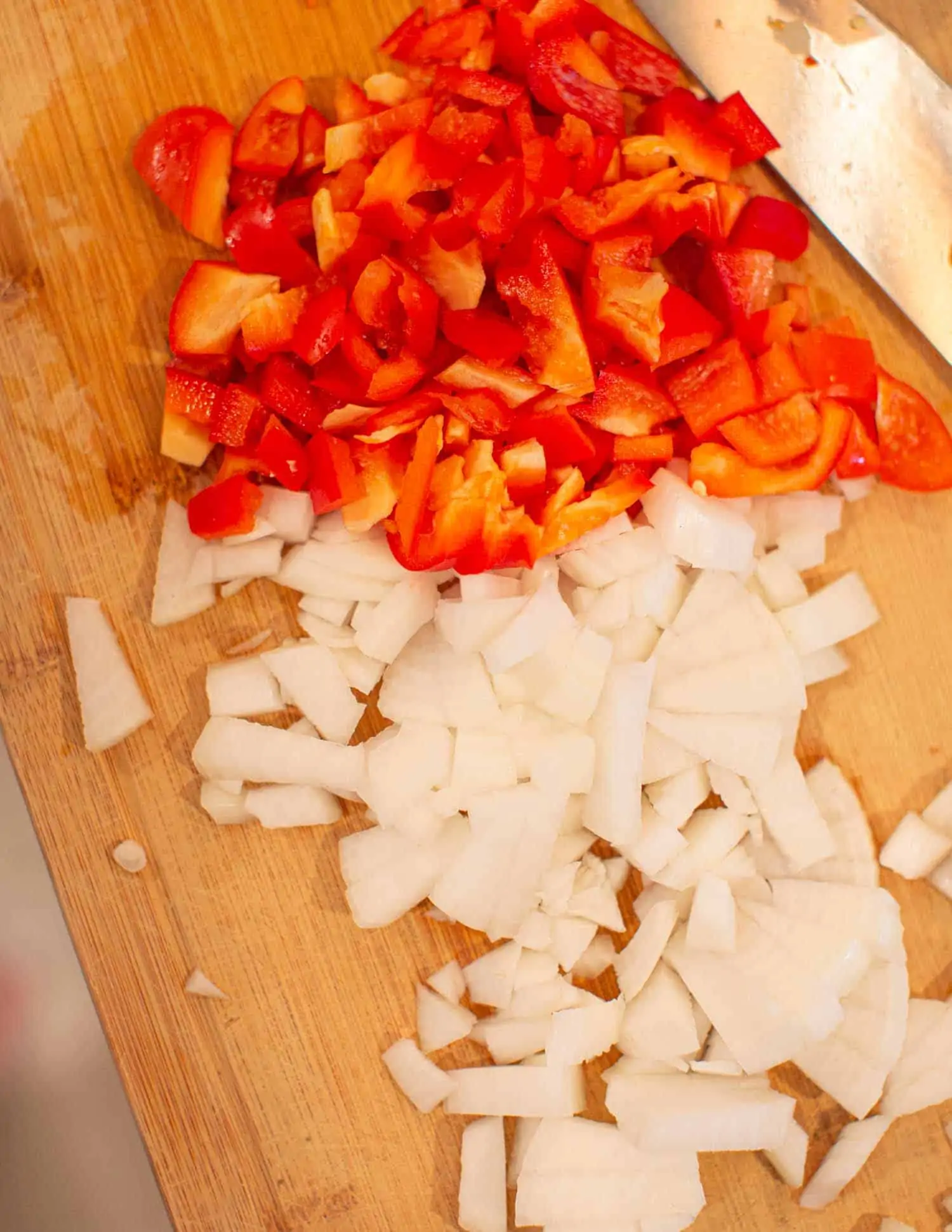 Chopped onion and bell pepper on a wooden cutting board.