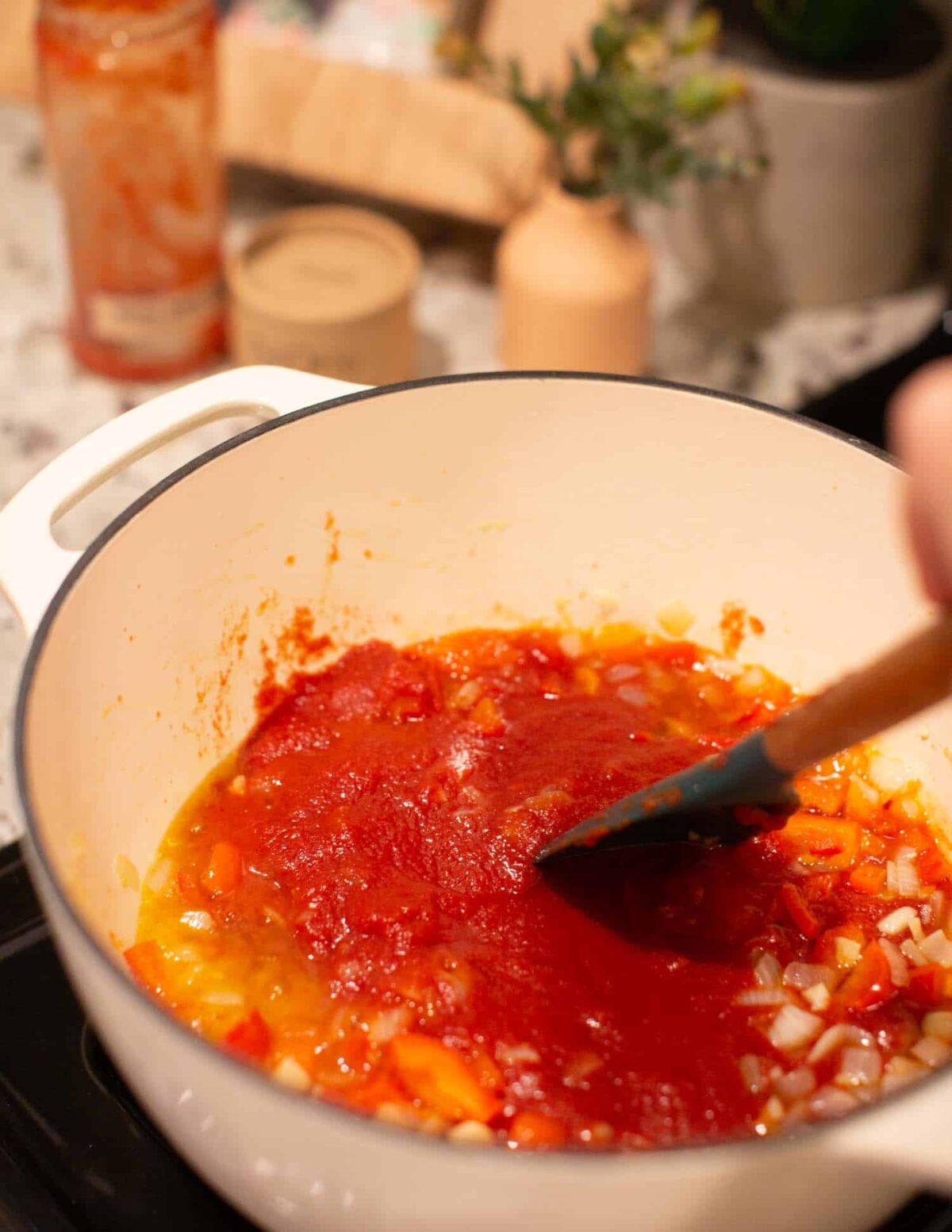 Tomatoes in sauce being added to a pot with sauteed veggies.