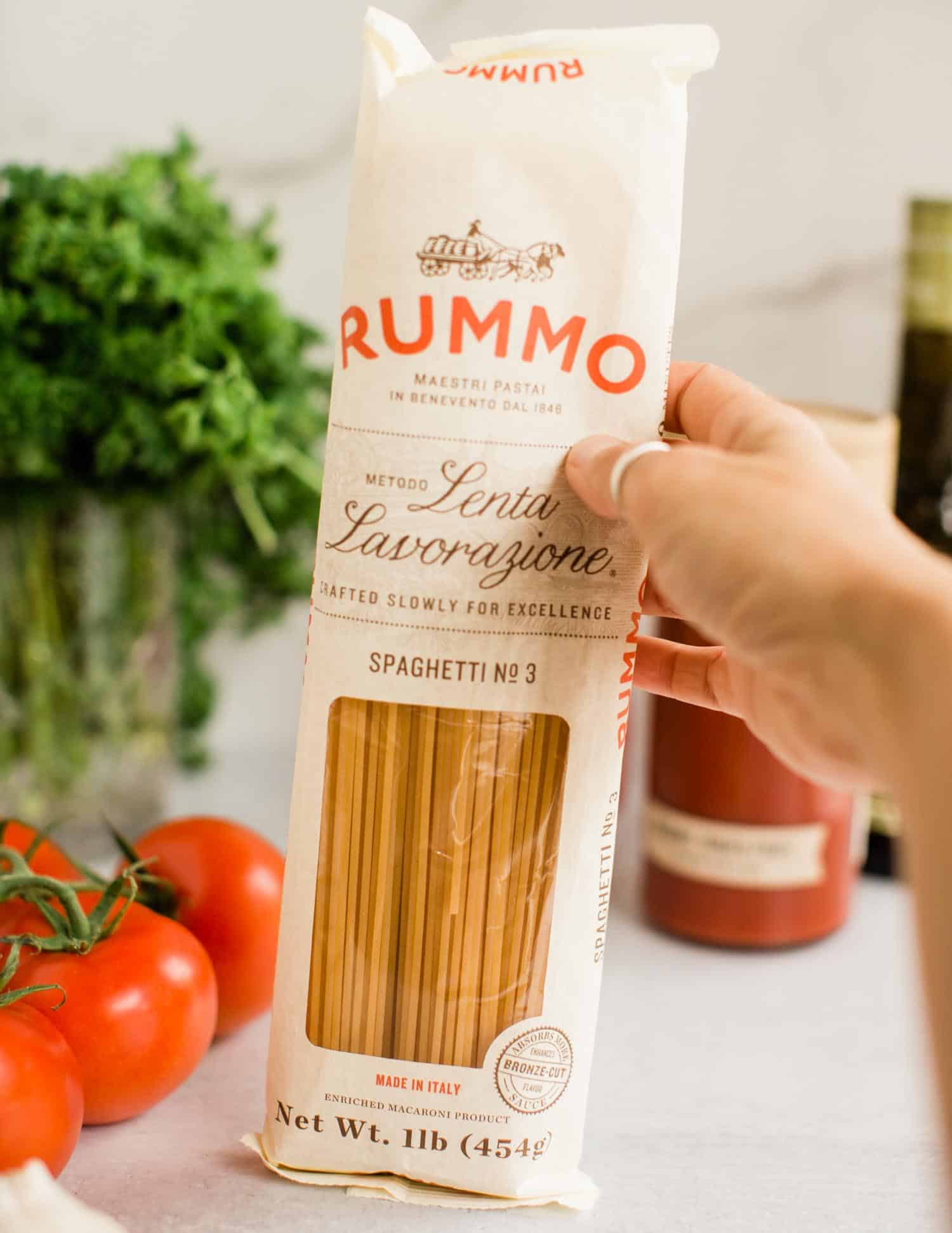 Package of dry spaghetti surrounded by fresh tomatoes, parsley, and classic Italian pasta ingredients.