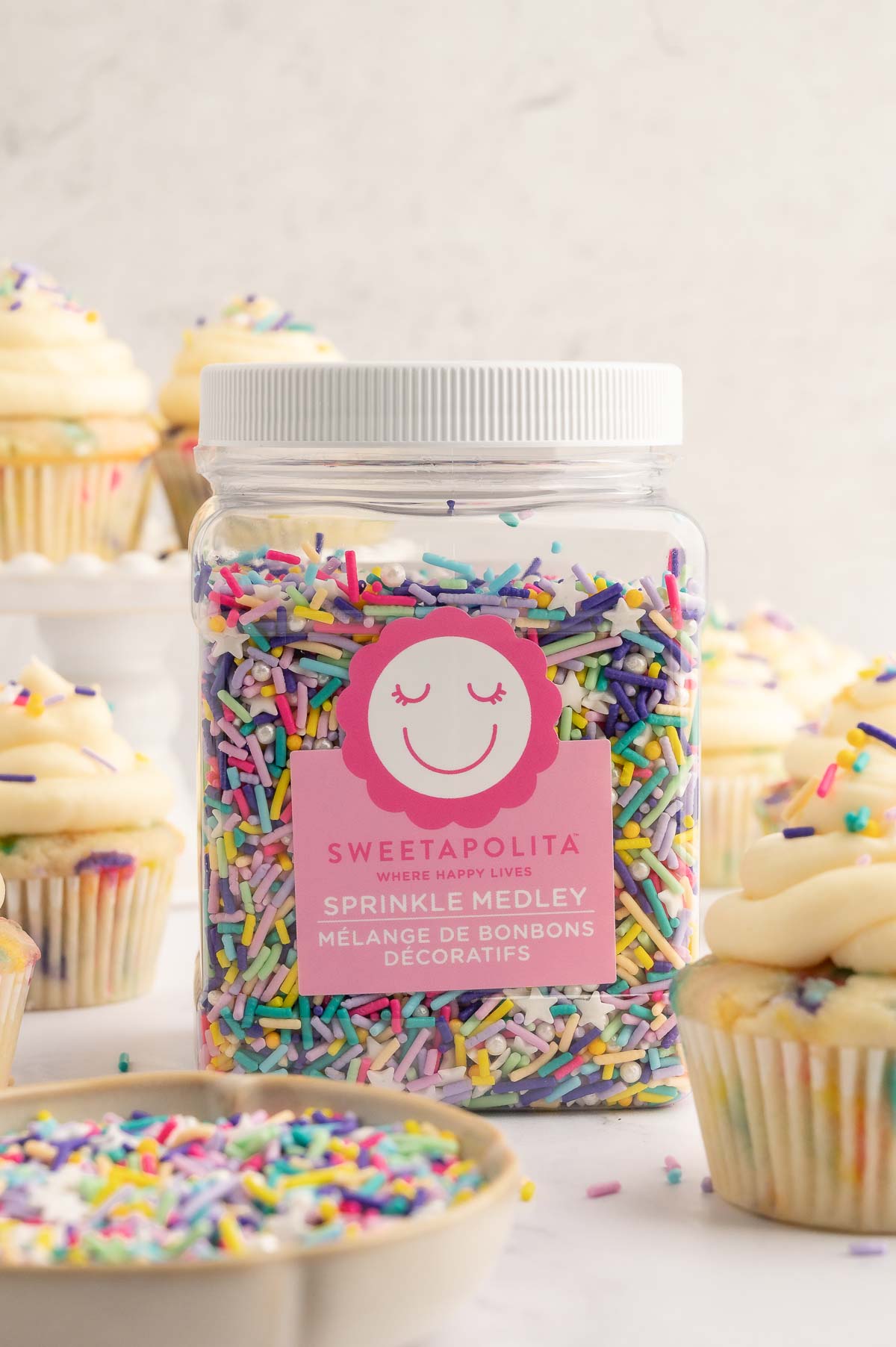 A jar of Sweetapolita vegan sprinkles next to cupcakes.
