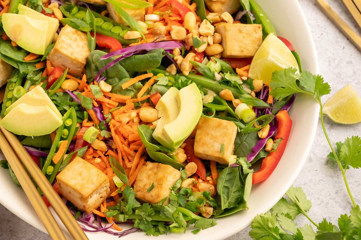 Close up of a Thai salad with colorful vegetables and cubed, marinated tofu in a white bowl.