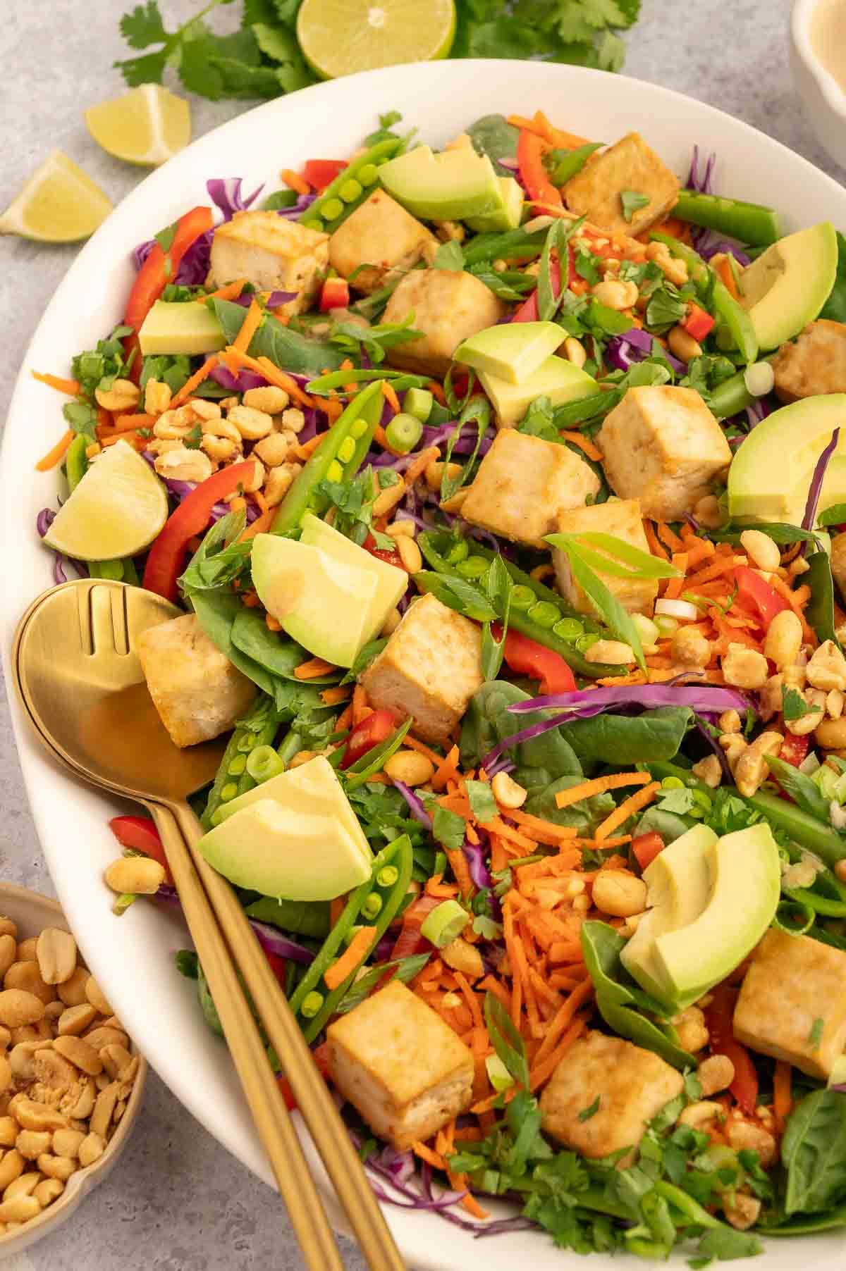 A close up of the finished Thai peanut salad with tofu in a shallow white bowl with gold forks.