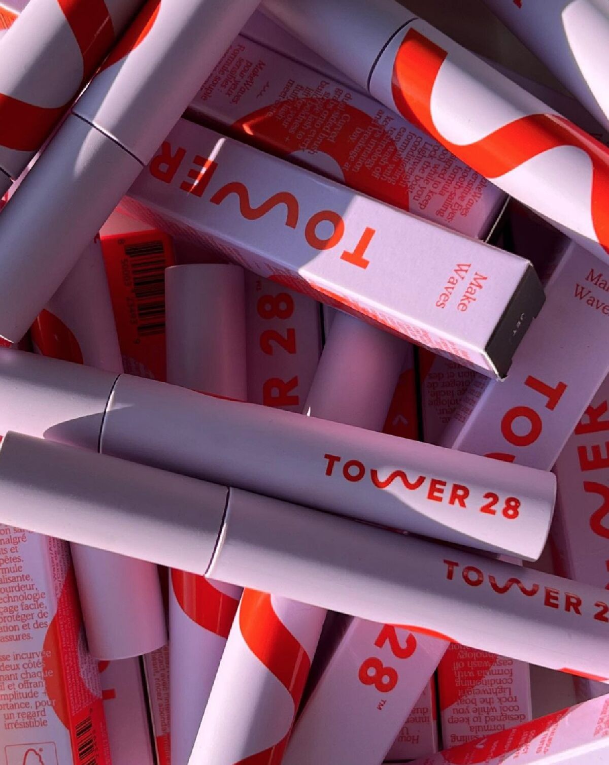 Assorted purple and red tubes and boxes of Tower 28 mascara in shadow and light.