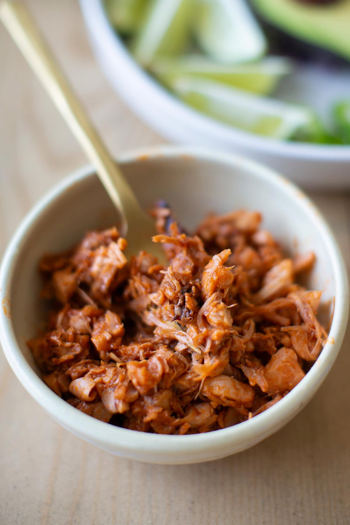 Close up of jackfruit taco meat with bbq sauce vegan-style in a white bowl with gold fork.