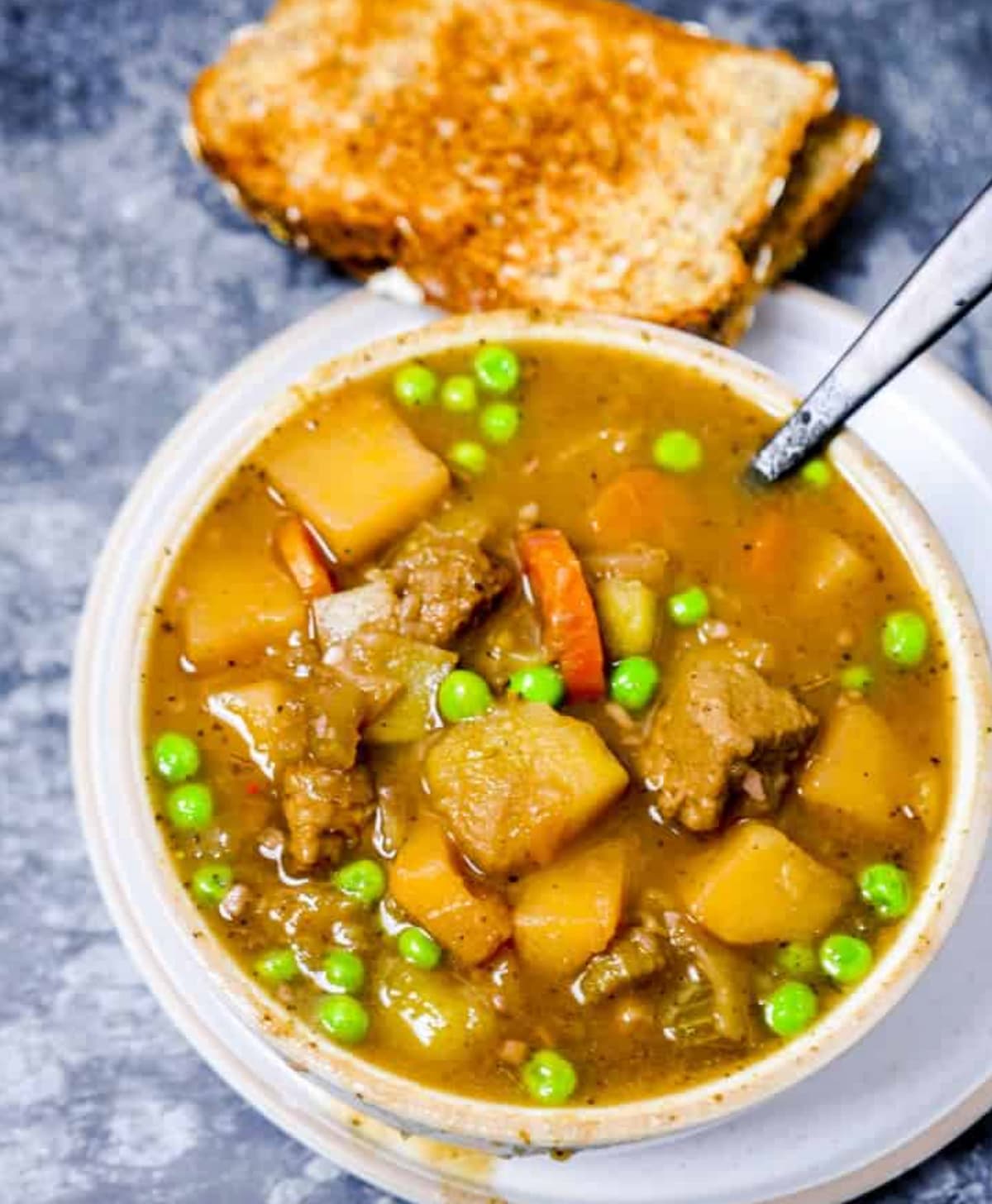 Vegan beef stew in a white bowl next to a slice of toast.