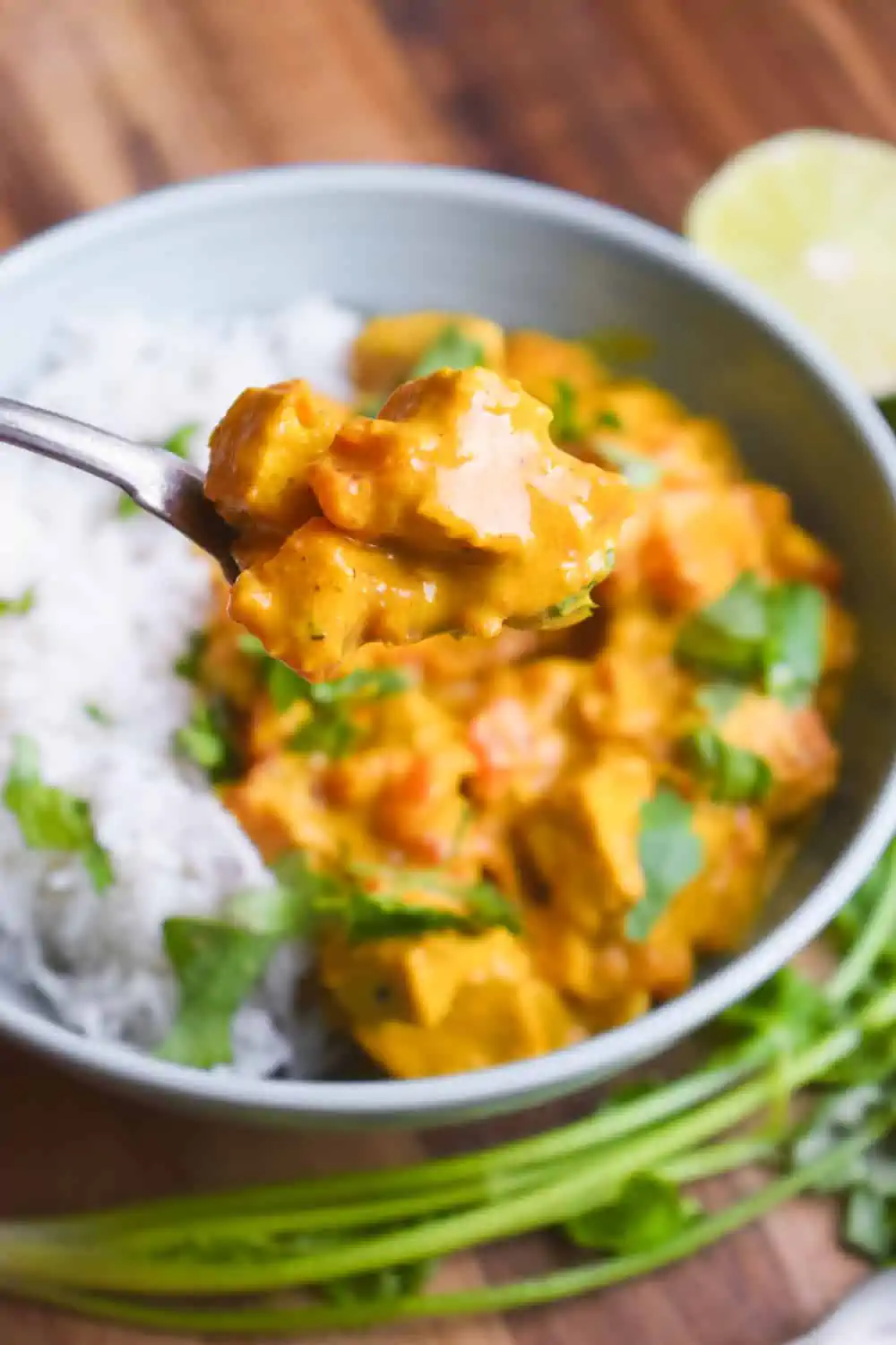 A spoon holding a bite of vegan butter chicken made with tofu.