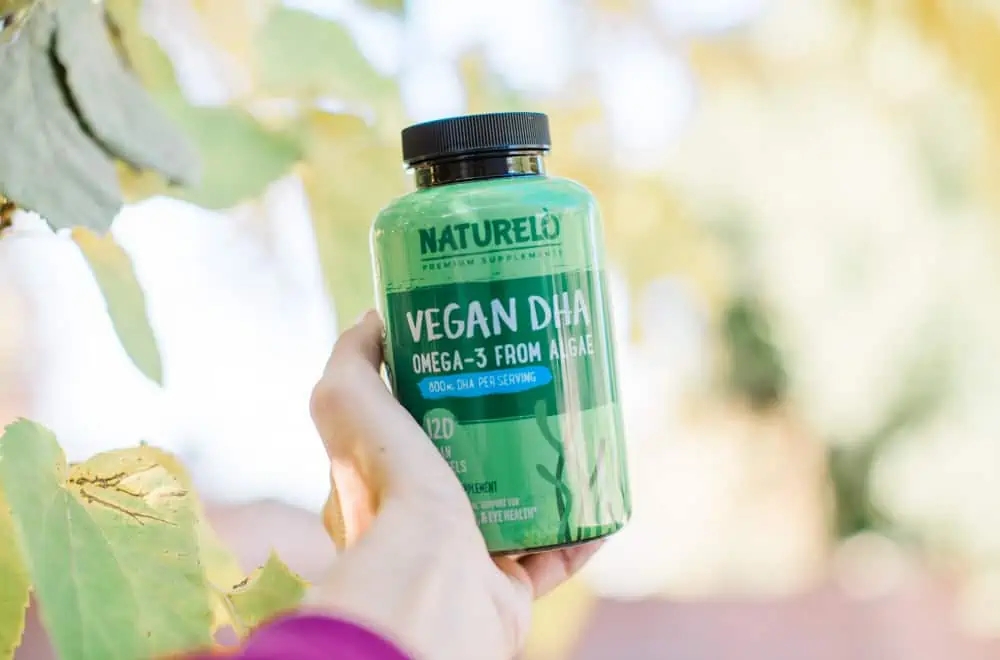 A hand holding a bottle of Naturelo Vegan DHA from an article titled, "How to Get Vegan DHA Without Fish Oil".