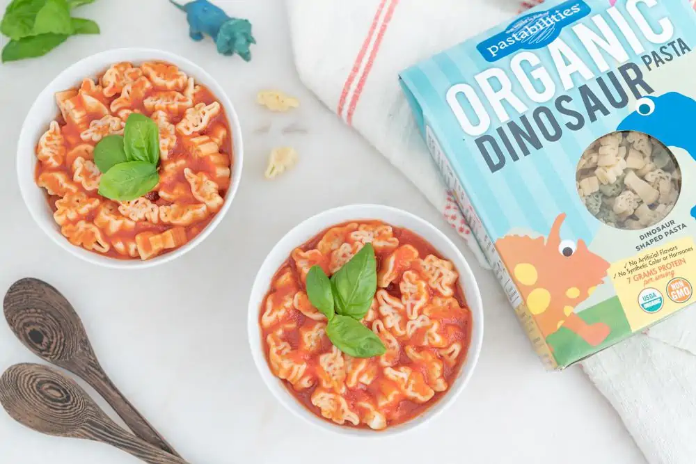 Two bowls of vegan Spaghettios made with fun dinosaur pasta shapes in tomato sauce.