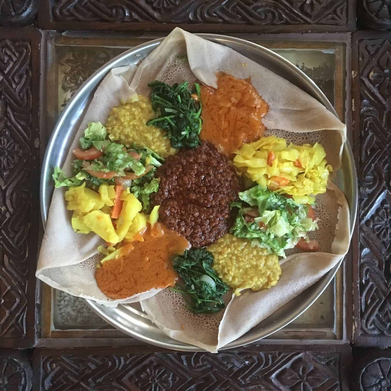 Ethiopian vegan cuisine with injera platter topped with lentil stews, split peas, and vegetables.