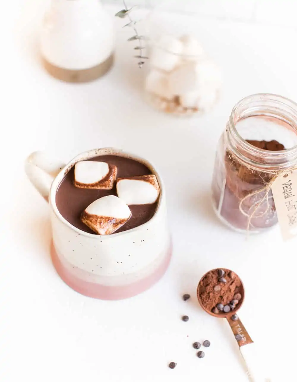 Vegan hot chocolate in a mug topped with marshmallows next to a jar of vegan hot cocoa mix.
