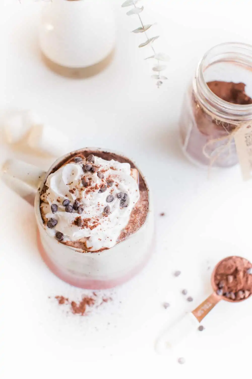 A mug of vegan hot cocoa topped with coconut whipped cream and mini vegan chocolate chips.