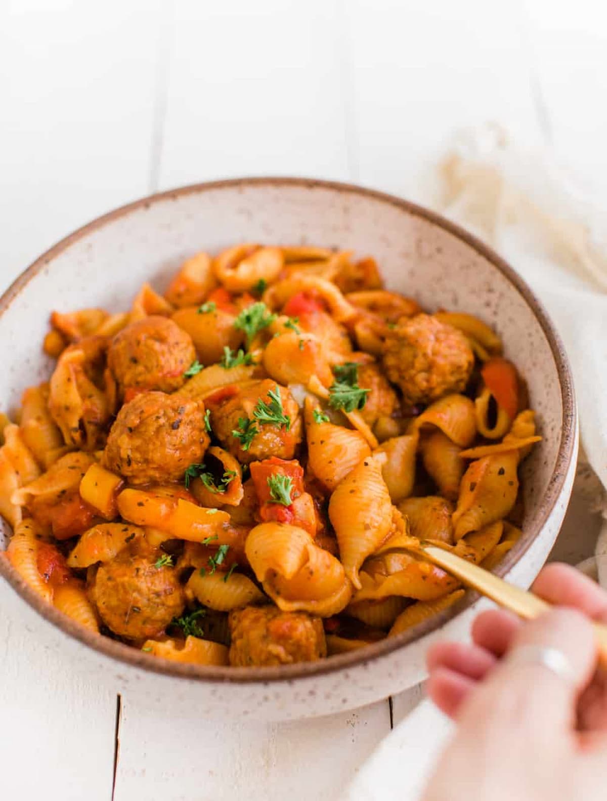 A hand holding a forkful of vegan instant pot pasta with meatballs in a bowl.