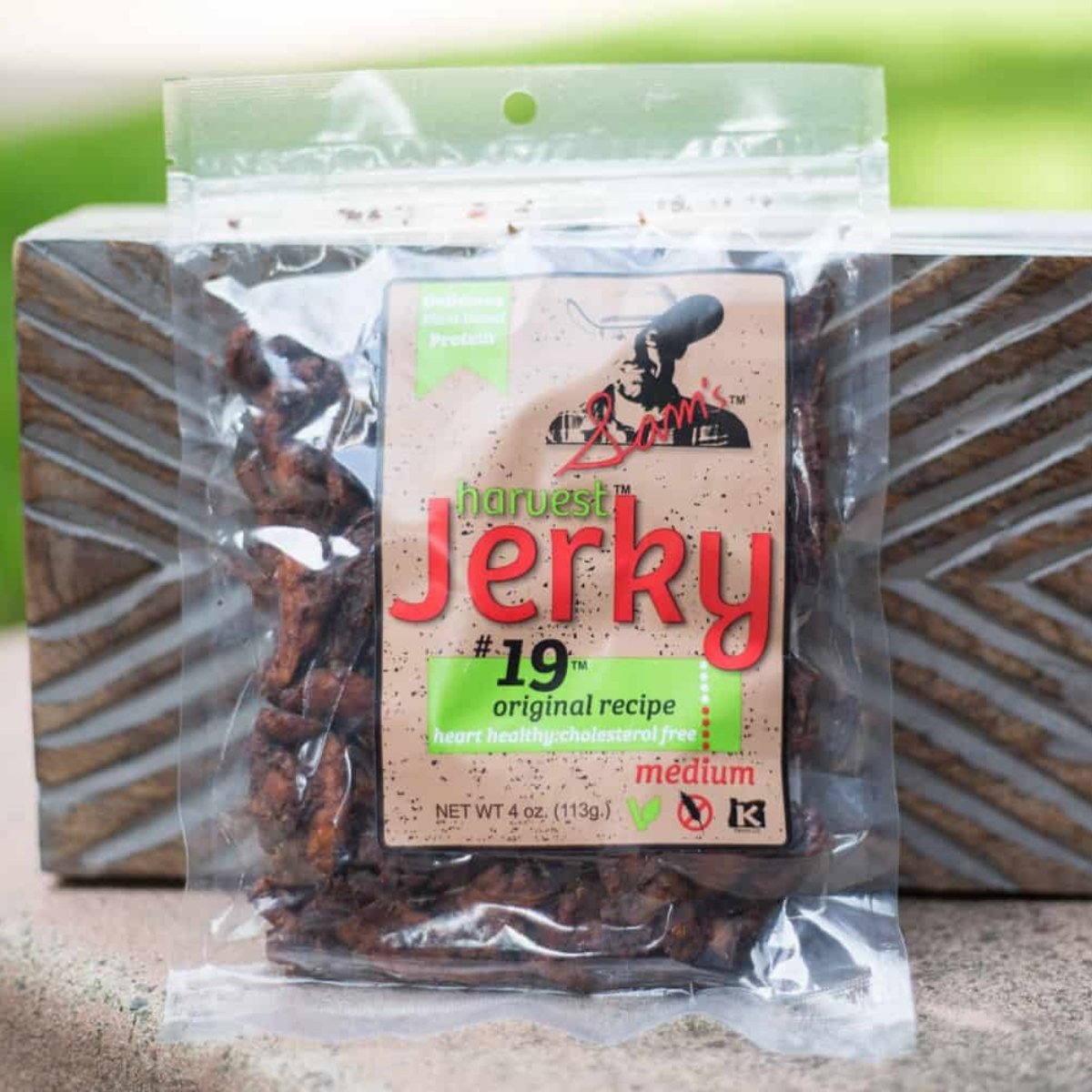 A clear plastic bag of vegan jerky standing up against a decorative brown wooden brick.
