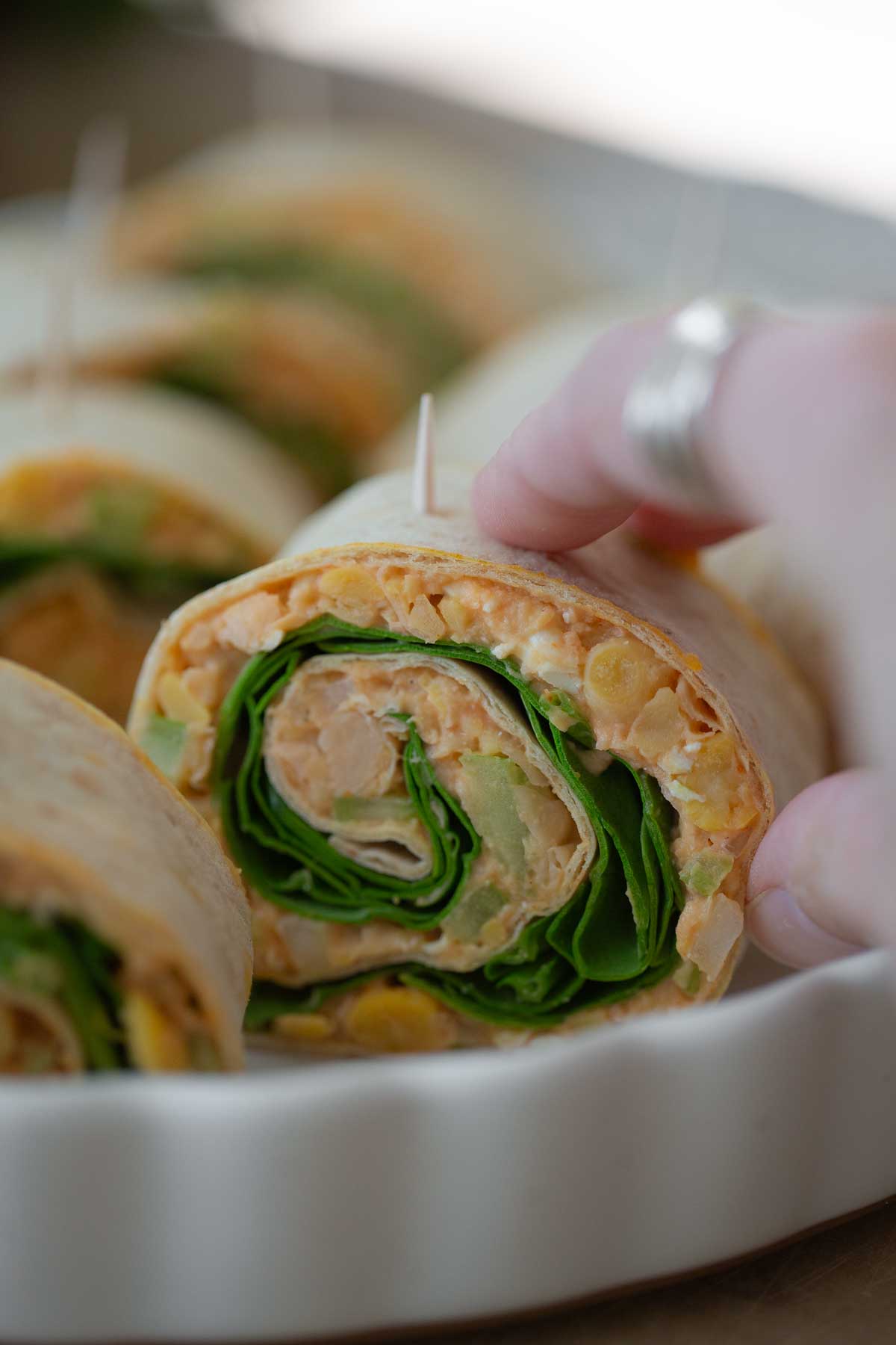 A hand grabbing a single vegan buffalo pinwheel sealed with a toothpick.