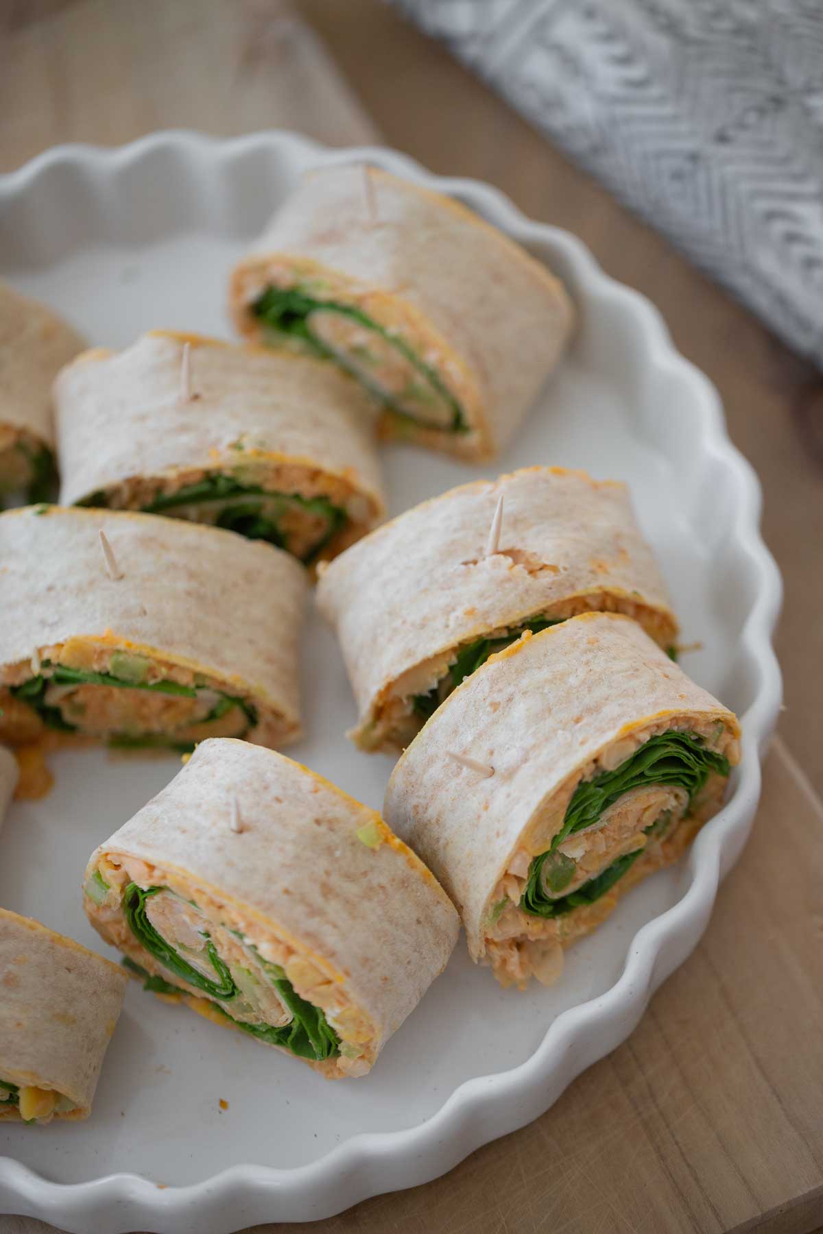 A top down view of a white baking dish with slices of vegan pinwheels stuffed with mashed chickpeas, hot sauce and spinach.