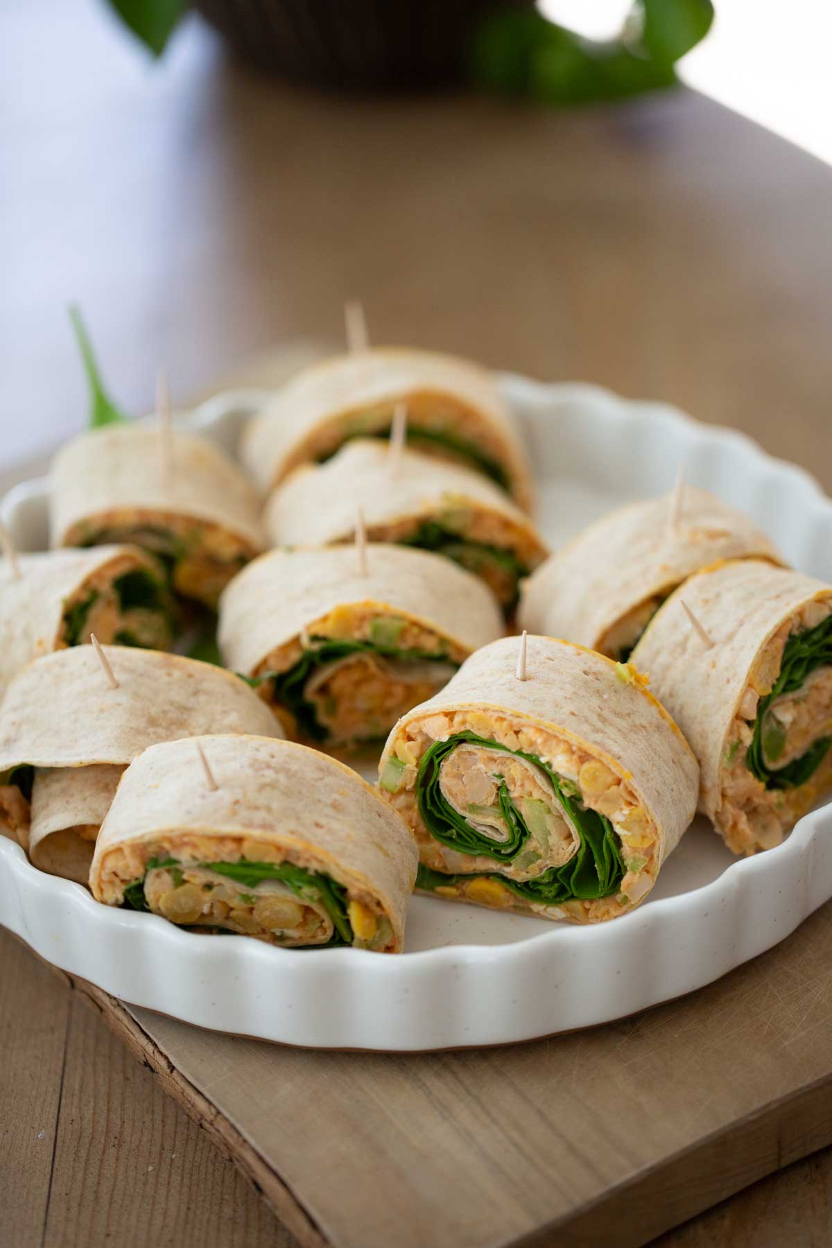 Ten vegan pinwheels with buffalo sauce, chickpeas and spinach arranged on in a white baking dish.