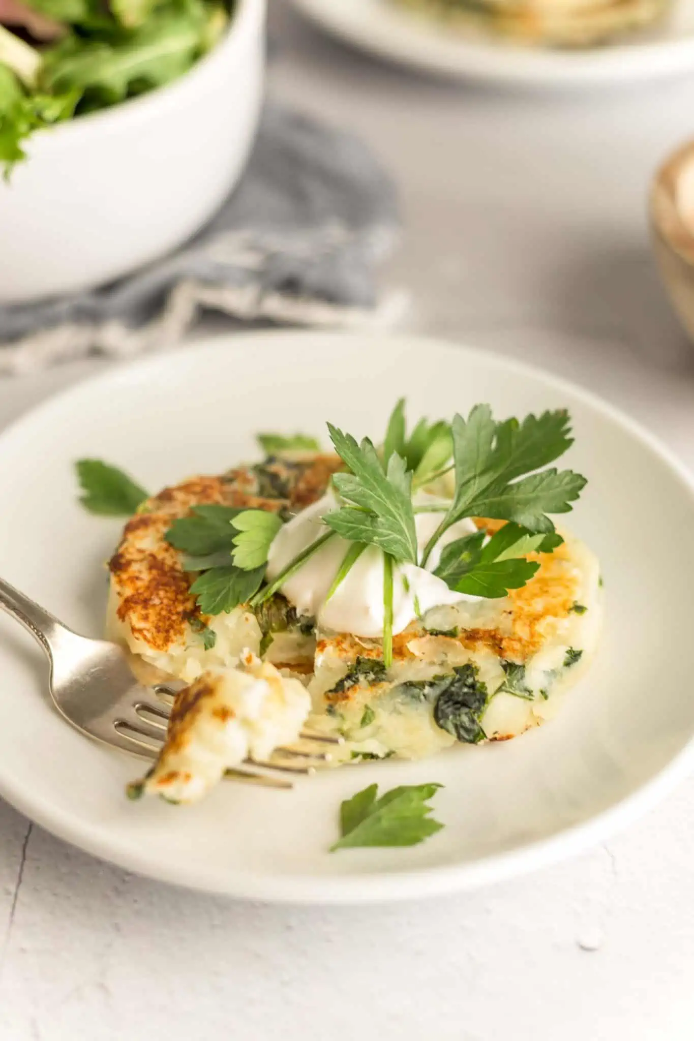 A close up photo of a vegan potato cake with fresh green herbs and vegan mayo on a white plate.