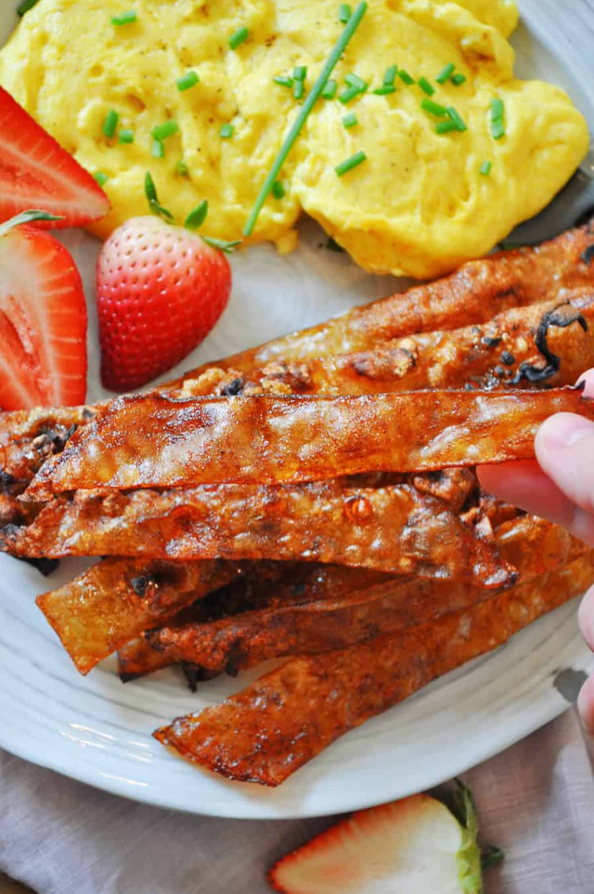 A white plate featuring vegan eggs, strawberries and vegan rice paper bacon by Rabbits & Wolves blog.
