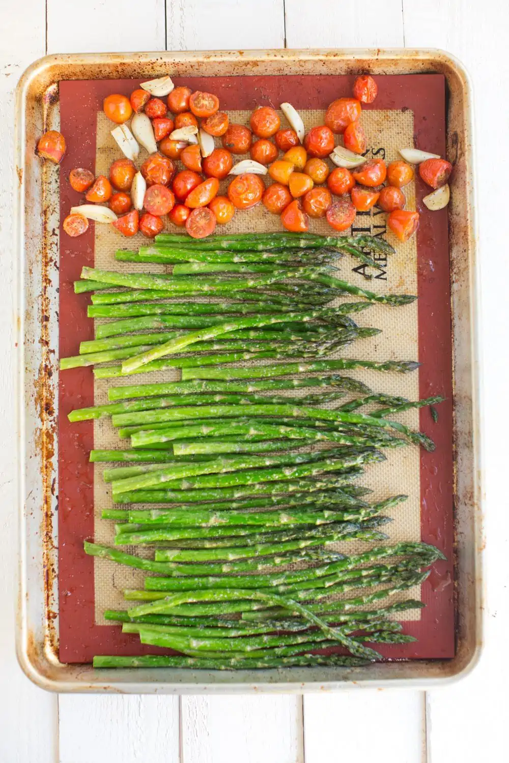 Asparagus, tomatoes, and garlic arranged on a line sheet pan.