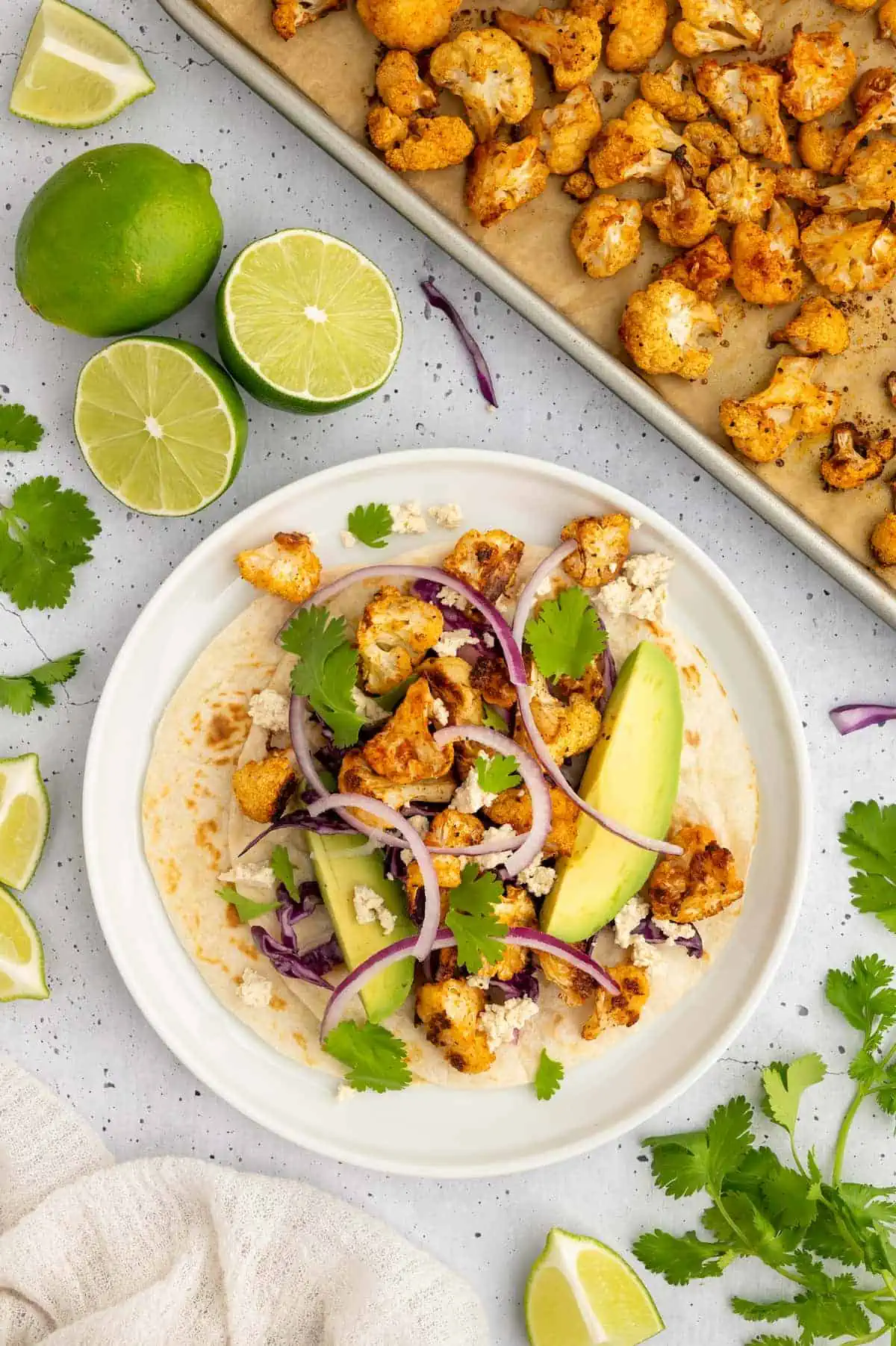 Fully assembled vegan cauliflower tacos with avocado, red onion, and fresh cilantro, served with lime wedges.