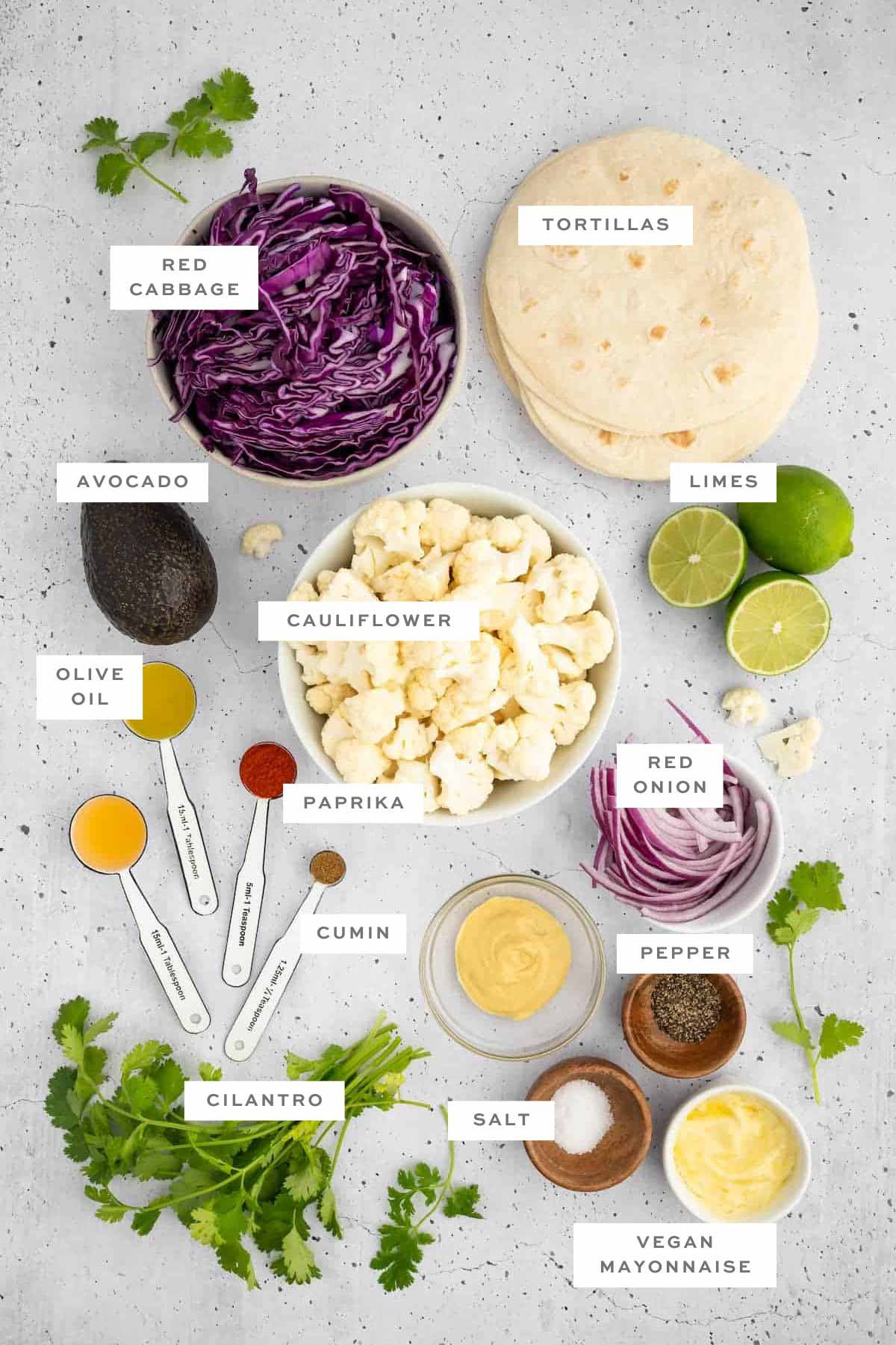Ingredients for vegan cauliflower tacos, including cauliflower, seasonings, cabbage, tortillas, and avocado, with labels.