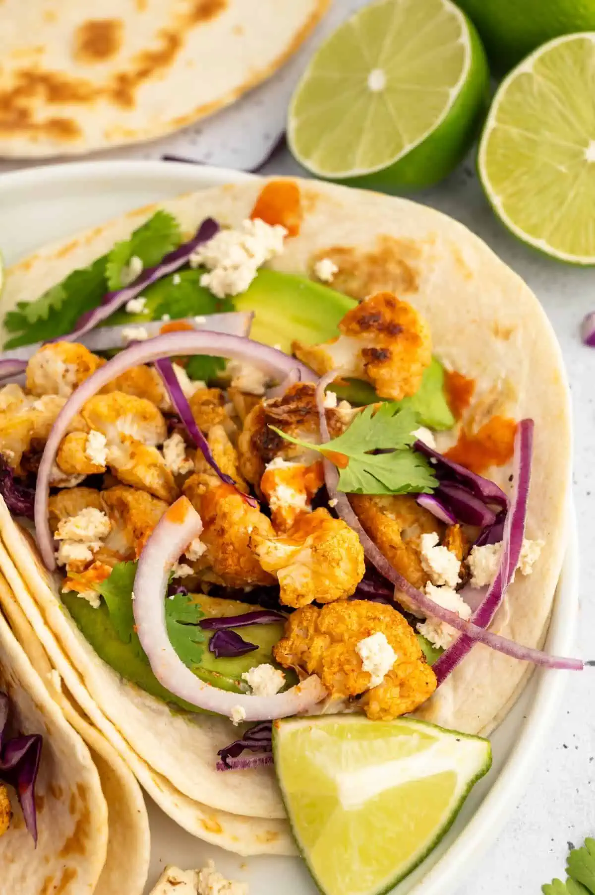 Close-up of vegan cauliflower tacos with crispy roasted cauliflower, slaw, avocado, and lime on soft tortillas.